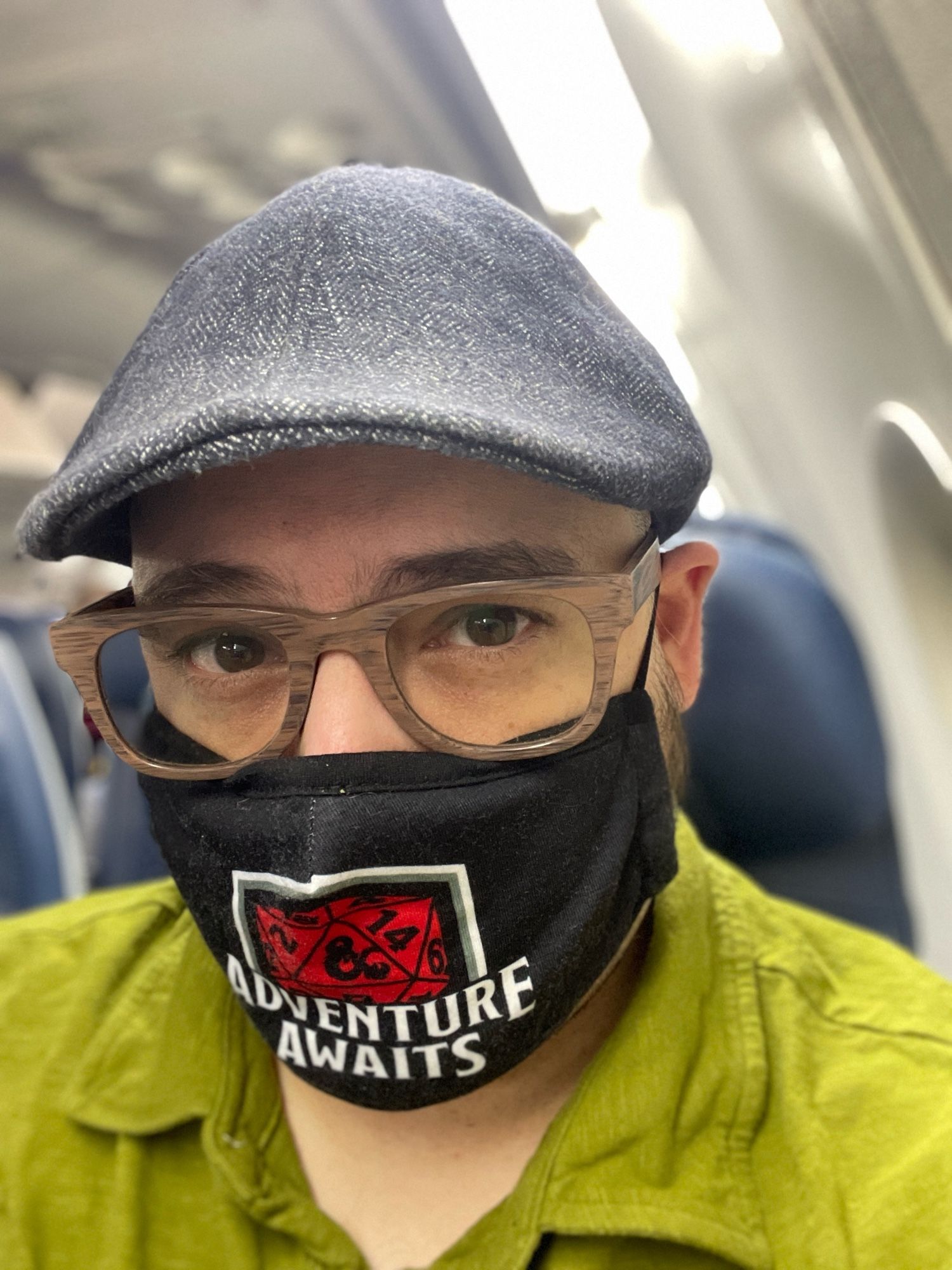 Just a guy in a mask that says Adventure Awaits sitting in a plane typing this description. My shirt is green, my glasses are wooden, my hat is grey… the world is waking up. Let’s gooooo!