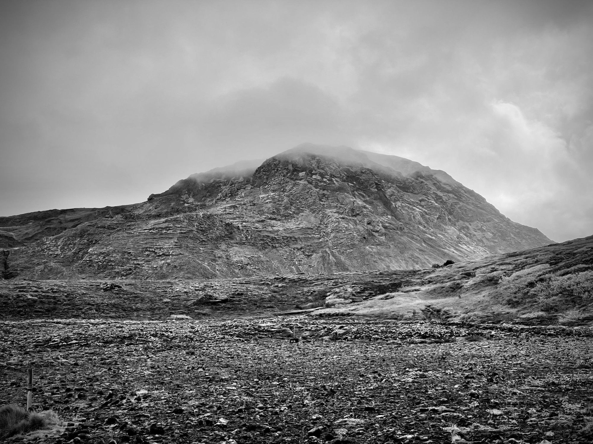 Black and white photo of Helgafell, Iceland; layered tephra mound with a cloud settling into the top