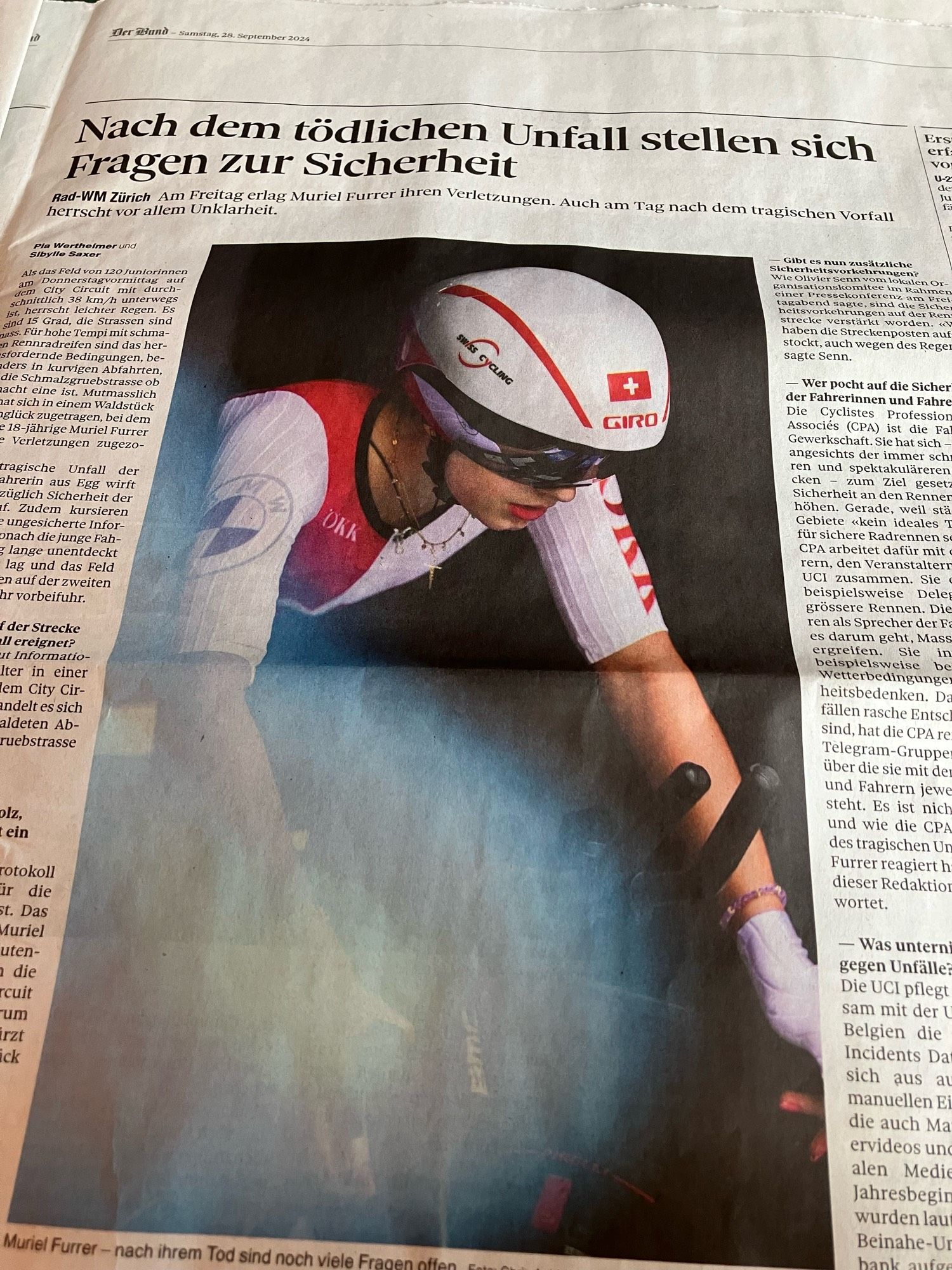 zeitungsausschnitt.
titel: Nach dem tödlichen Unfall stellen sich
Fragen zur Sicherheit
lead: Rad-WM Zürich [fett] Am Freitag erlag Muriel Furrer Ihren Verletzungen. Auch am Tag nach dem tragischen Vorfall herrscht vor allem Unklarheit.
[grosses bild. junge frau mit rotem lippenstift und goldkettchen im kurzarm-velo-dress von rechts vorne. sie sitzt in rennpose auf dem rennrad. dress und helm in weiss/rot. werbelogos auf dem dress. eine schweizer flagge vorne auf dem helm. goldkettchen mit kreuz. schwarz verspiegelte sonnenbrille.
hintergrund ist ganz schwarz.
von links unten ein weiss-bläulicher blurring-fleck über rechter unterarm und hand.]
lauftext besteht aus fragen und antworten.
oben rechts der seite: der bund