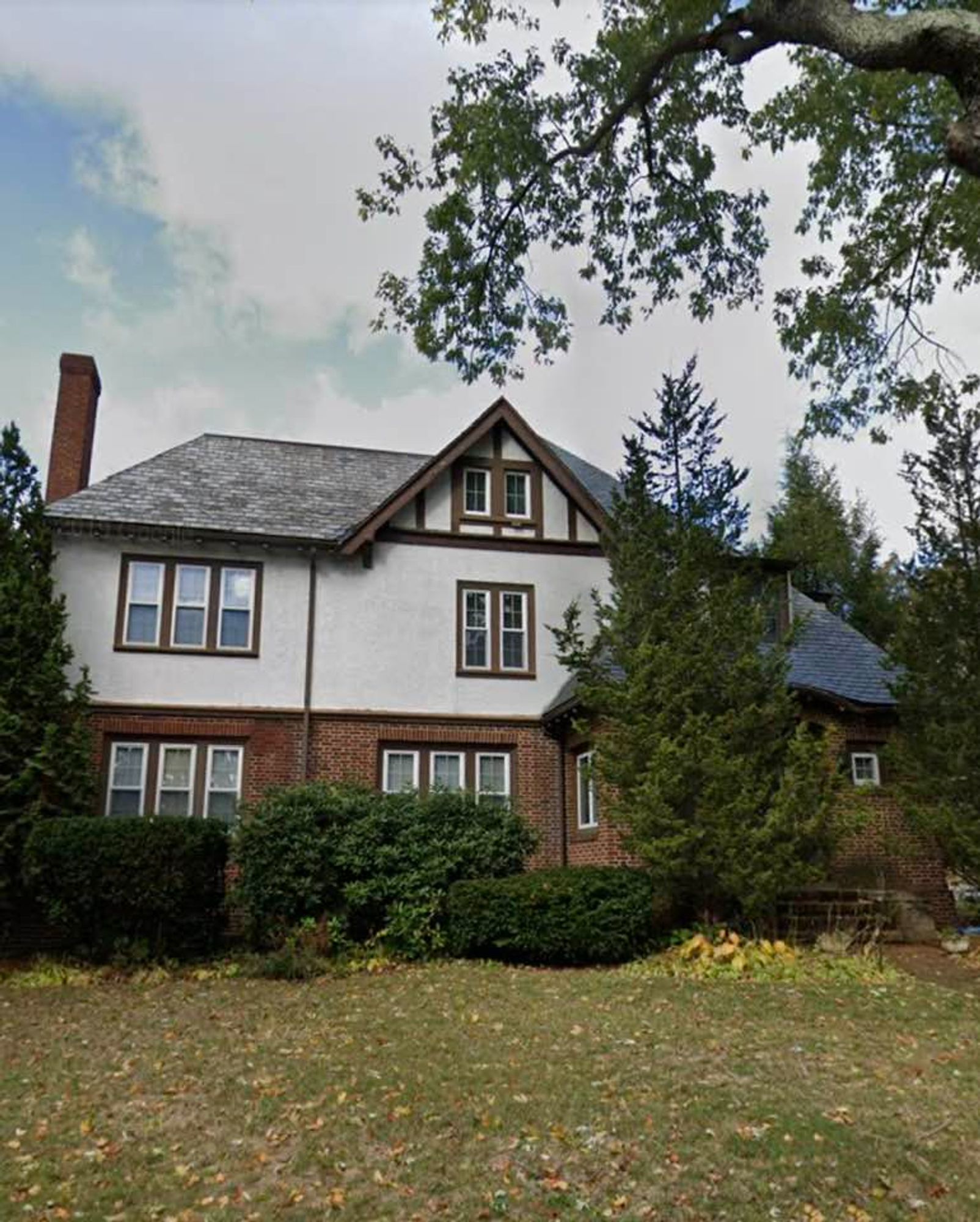 Photo of a very grand, imposing looking 3 story brick & stucco house. There are 15 windows visible on the front of the house. The roof is slate, the downspouts are copper, and there is a very tall brick chimney.