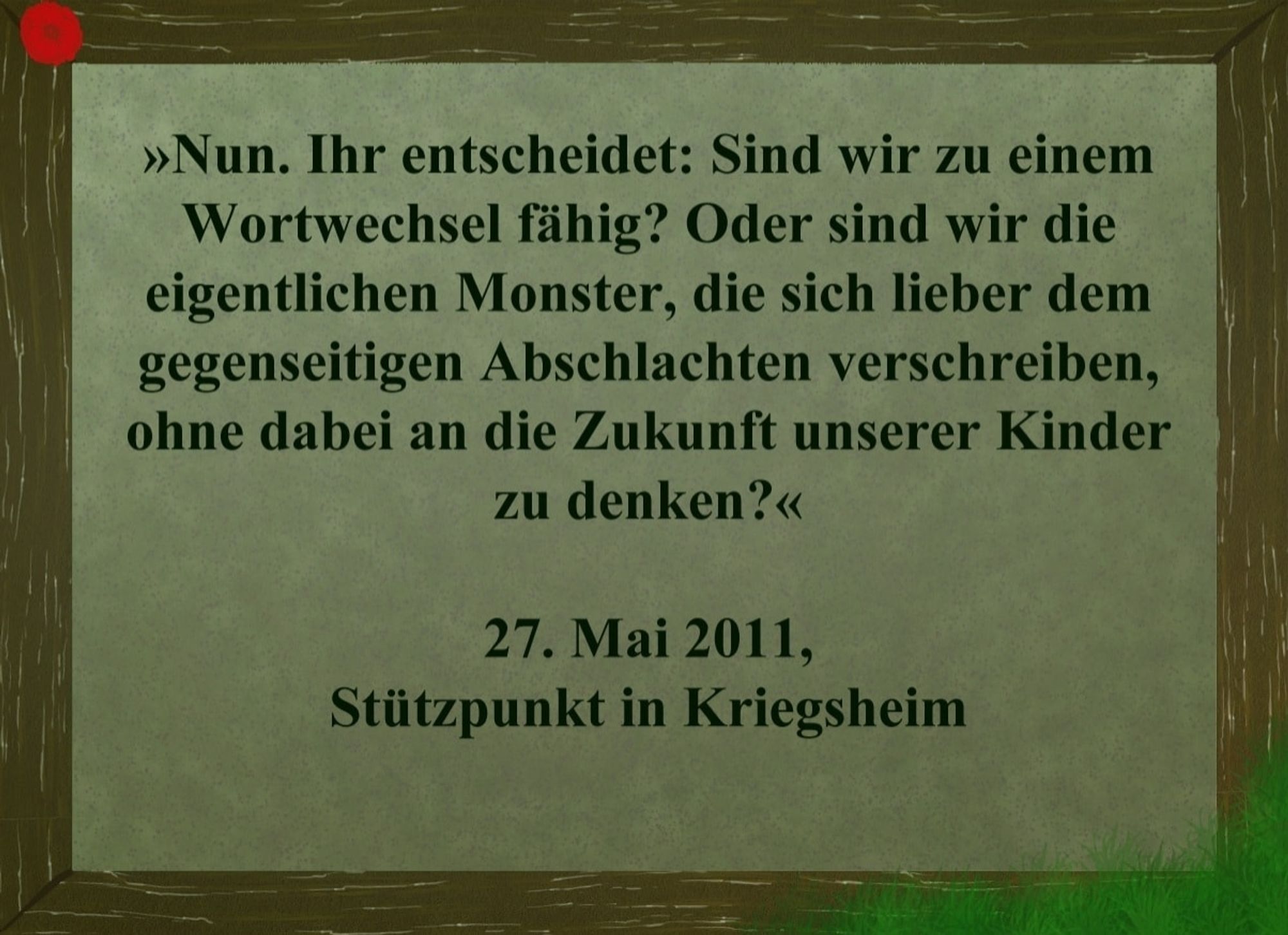 Text auf einem Bilderrahmen mit Mohnblume an der Ecke: "Nun. Ihr entscheidet: Sind wir zu einem Wortwechsel fähig? Oder sind wir die eigentlichen Monster, die sich lieber dem gegenseitigen Abschlachten verschreiben, ohne dabei an die Zukunft unserer Kinder zu denken?" 27. Mai 2011, Stützpunkt in Kriegsheim