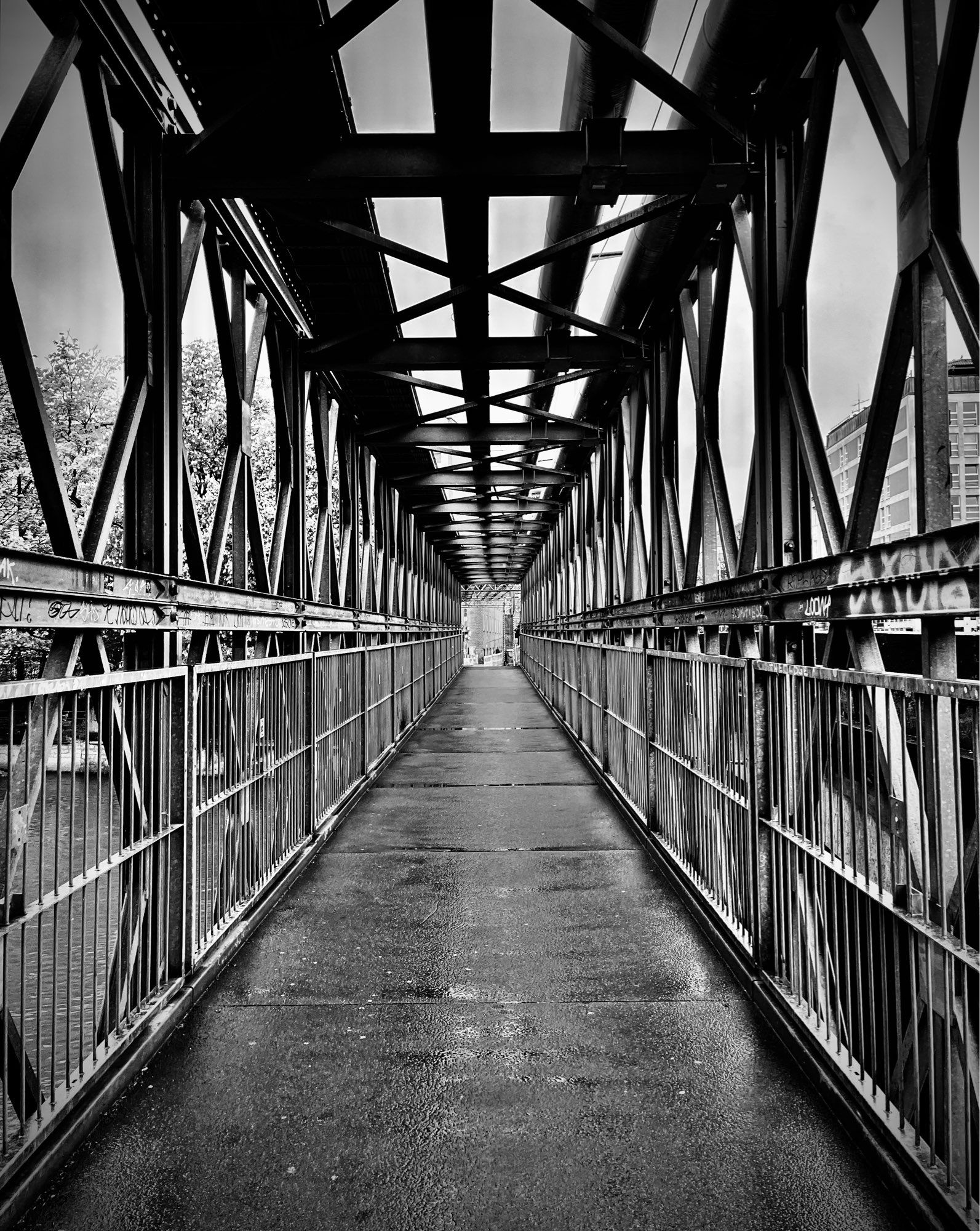 S/W-Foto. Zentraler Blick auf eine Fußgängerbrücke aus Stahl. Unzählige teilweise diagonale Stahlstreben auch über Kopf bilden ein Muster und laufen zum anderen Brückenende fluchtpunktartig zusammen