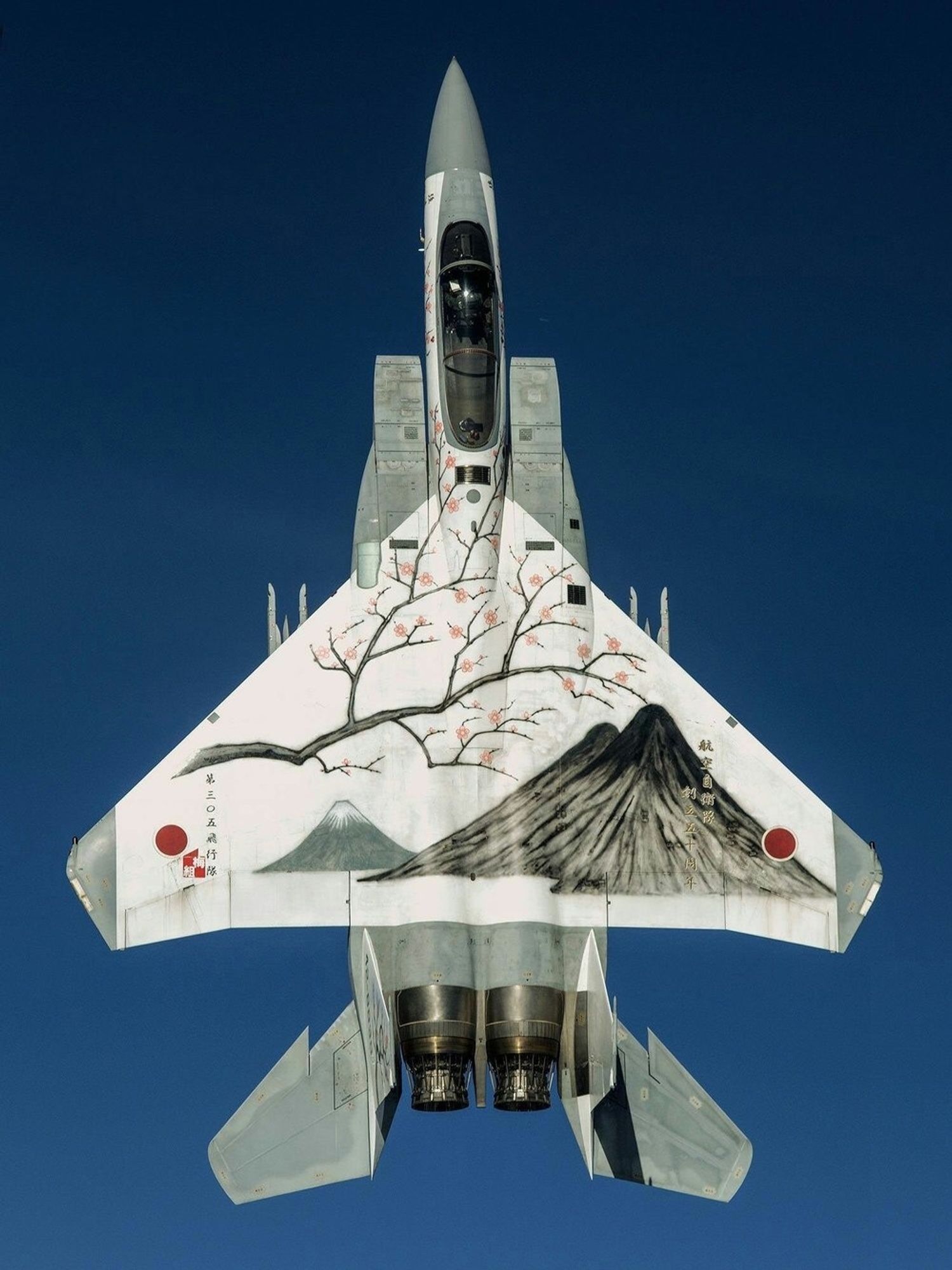 In the picture, the fighter jet against the blue sky, flies vertically upwards and Mount Fuji is painted on the wings of the fighter jet.