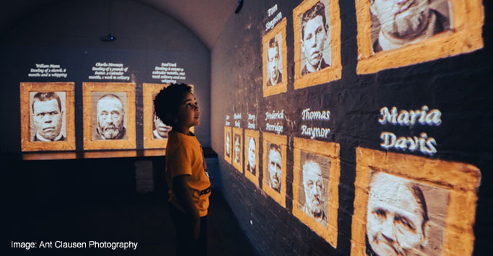 A young boy looking at faces projected on a wall.