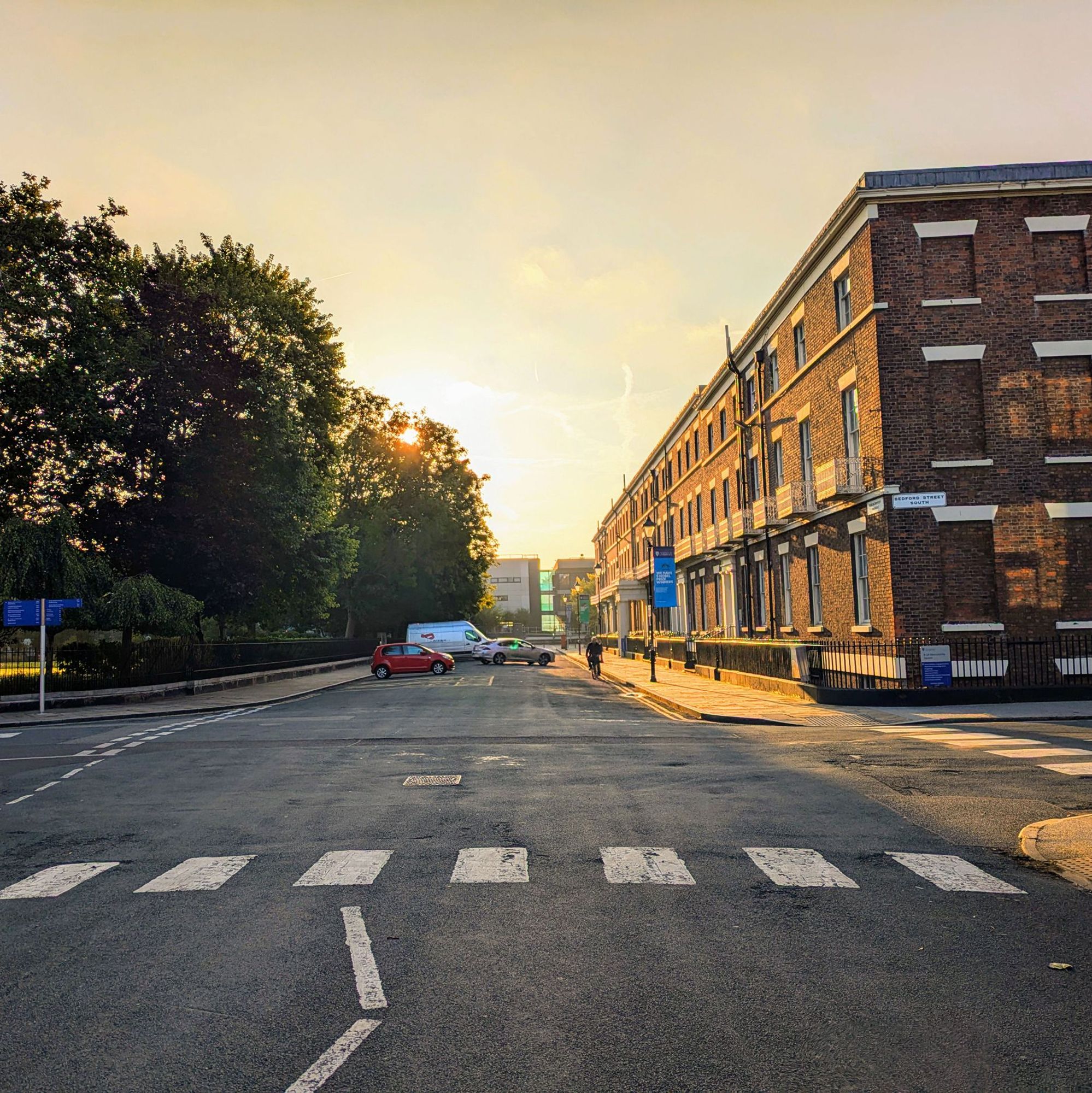 A photo looking east across the south side of Abercromby Square towards the rising sun, a zebra crossing visible in the foreground. Both fab and gear.