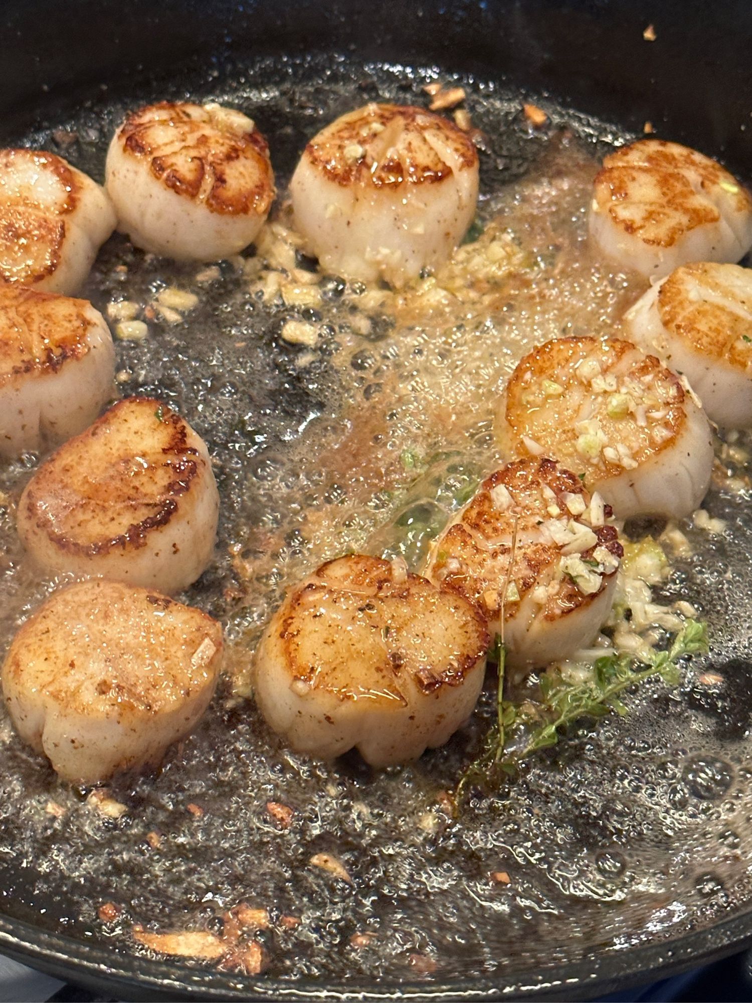 Scallops being cooked in a pan with butter garlic and thyme 