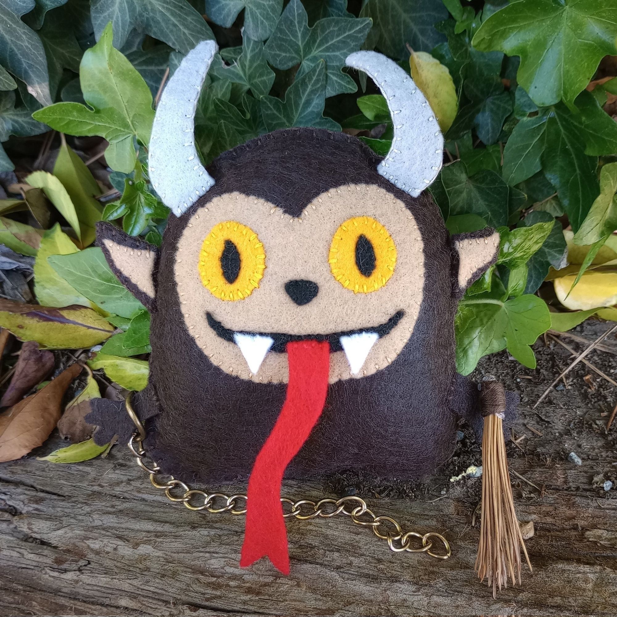 Here's a photo of a fabric art Krampus. He has yellow eyes, sharp teeth, and a long red tongue. He has a little chain and a bundle of sticks.