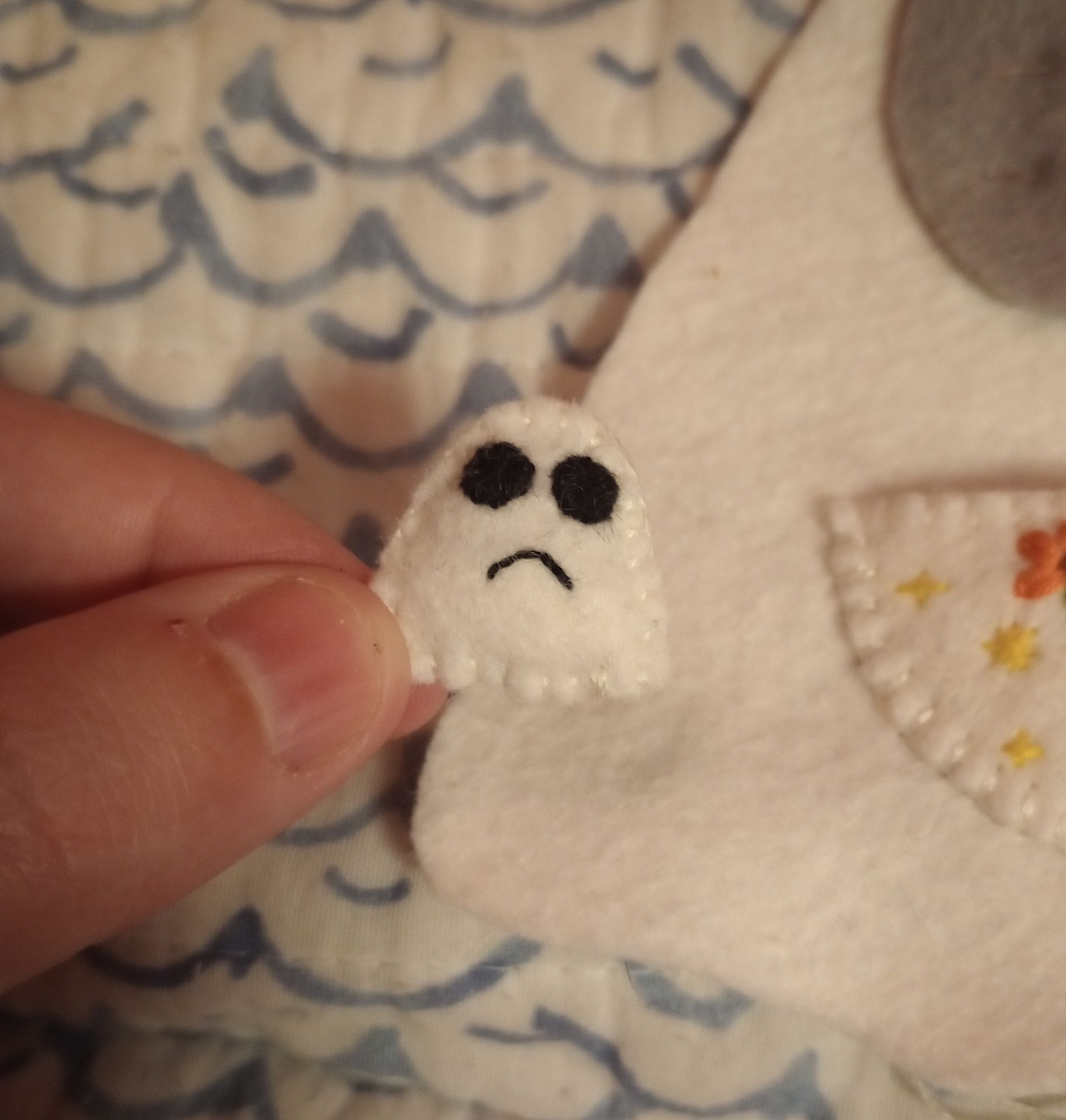 Here's a photo of me holding my tiny fabric art ghost between two fingers. She is very small. She has black eyes and a little frown.