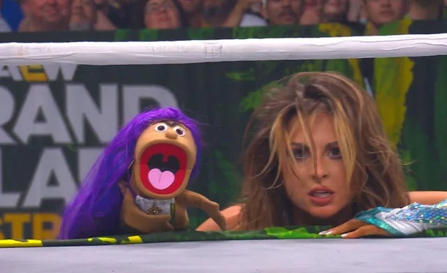 Harley Cameron and puppet Michelle Mone staring intently under the bottom rope. Harley looks dishevelled and puppet Michelle is visibly furious