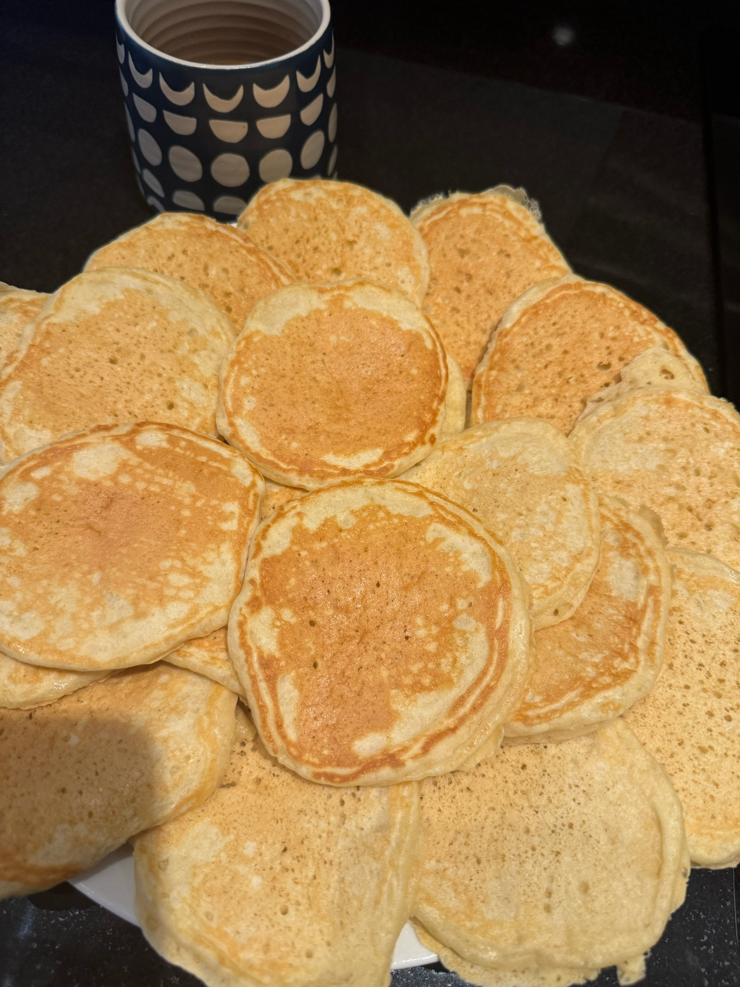 A cup of coffee next to a pile of two dozen pancakes.