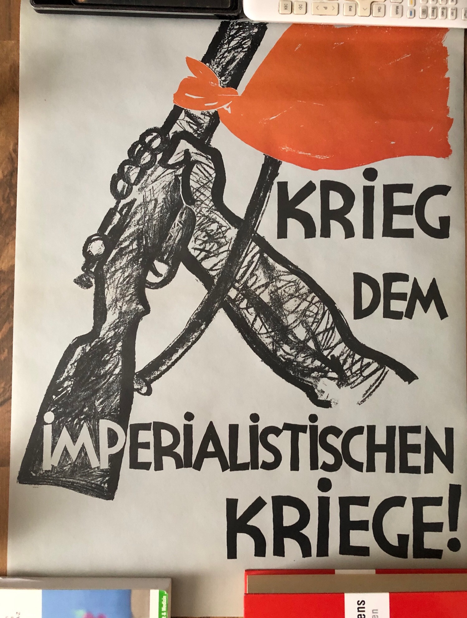 Plakat der KPD. Auf hellem pastellbeigen Hintergrund steht in schwarzer Schrift “Krieg dem Imperialistischen Kriege!” 
Ein ausgestreckter Arm hebt triumphierend ein Gewehr, an welches eine rote Fahne gebunden wurde, empor.”