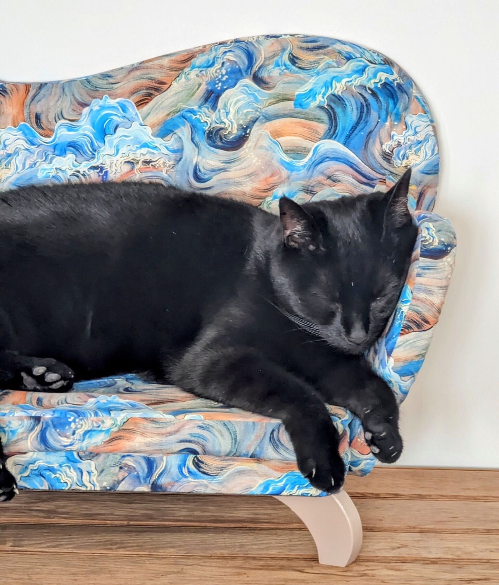 Black cat sleeping soundly in a blue cat sofa