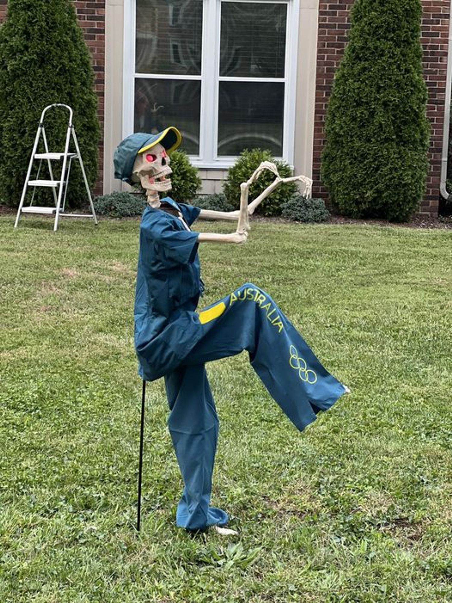 Uma caveira de plástico usando uma roupa similar à da australiana que disputou a competição de Break Dance nas Olimpíadas de Paris em um gramado de uma casa americana