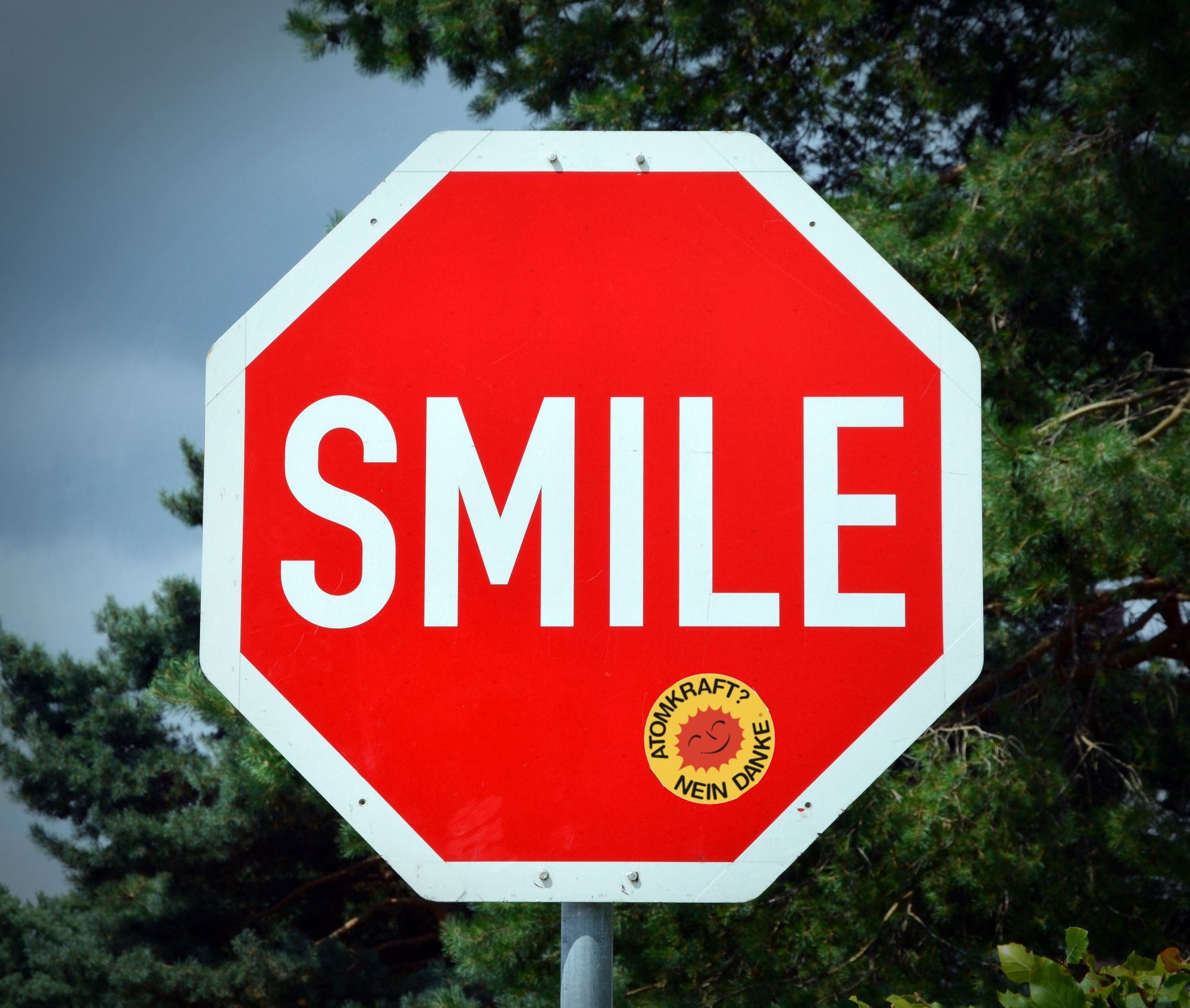 Ein achteckiges rotes Stoppschild auf dem mit großen Lettern Smile steht. Unter dem Wort Smile klebt ein Atomkraft nein danke Aufkleber.