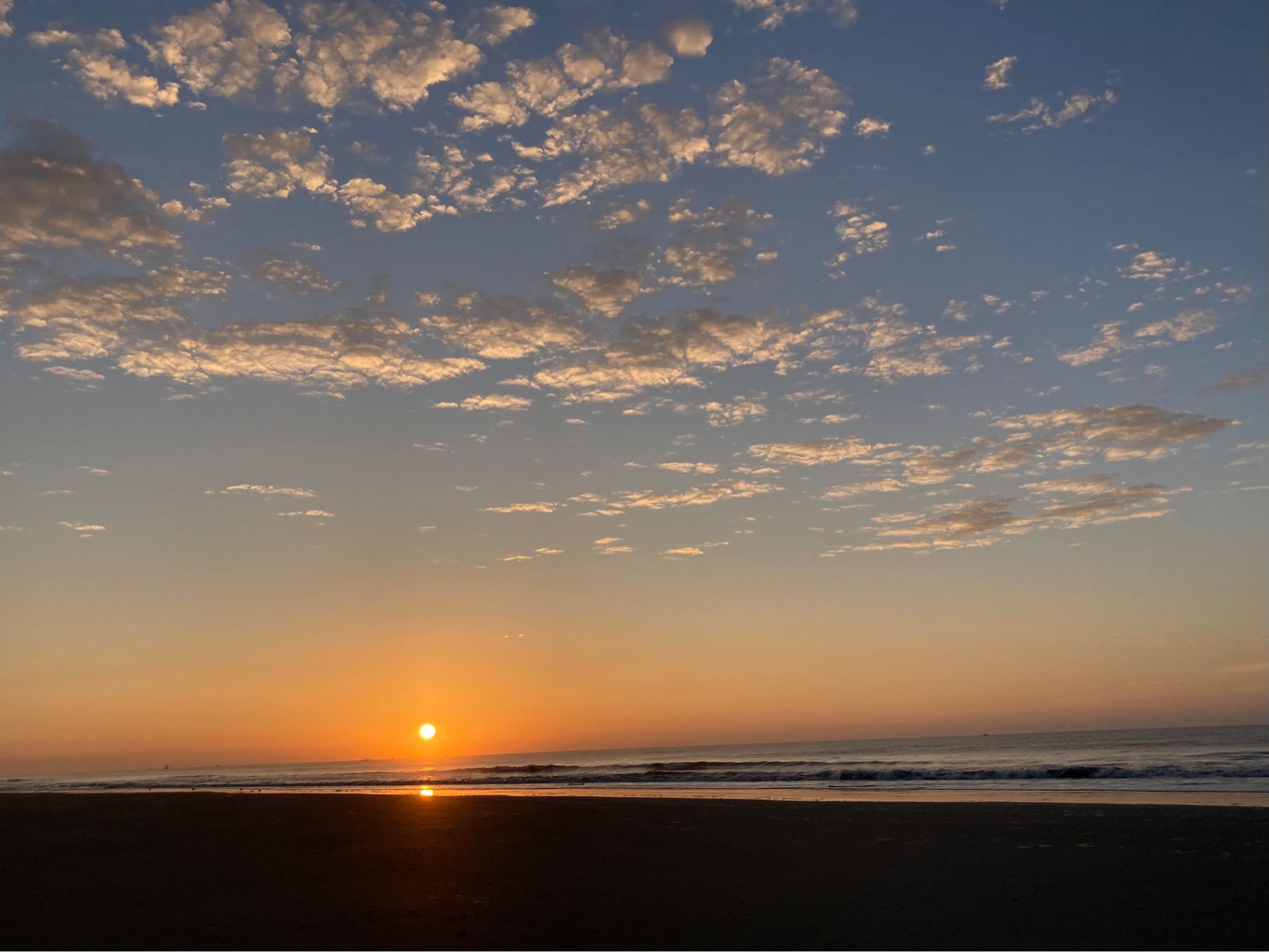 The sun rising I’ve the ocean. A scattering of small clouds are illuminated from below.