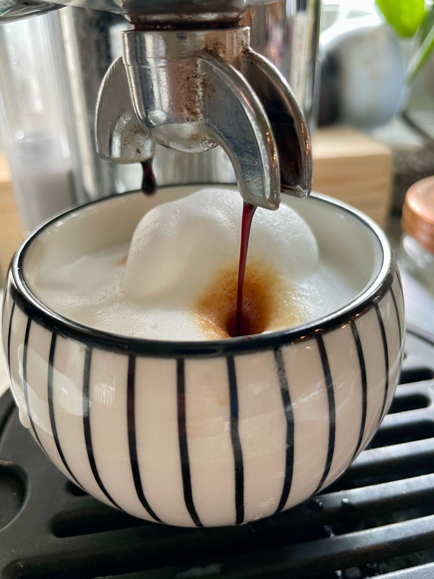 Espresso läuft aus der Handhebelmaschine in einen kleinen schwarzweiß gestreiften Becher mit Milchschaum.