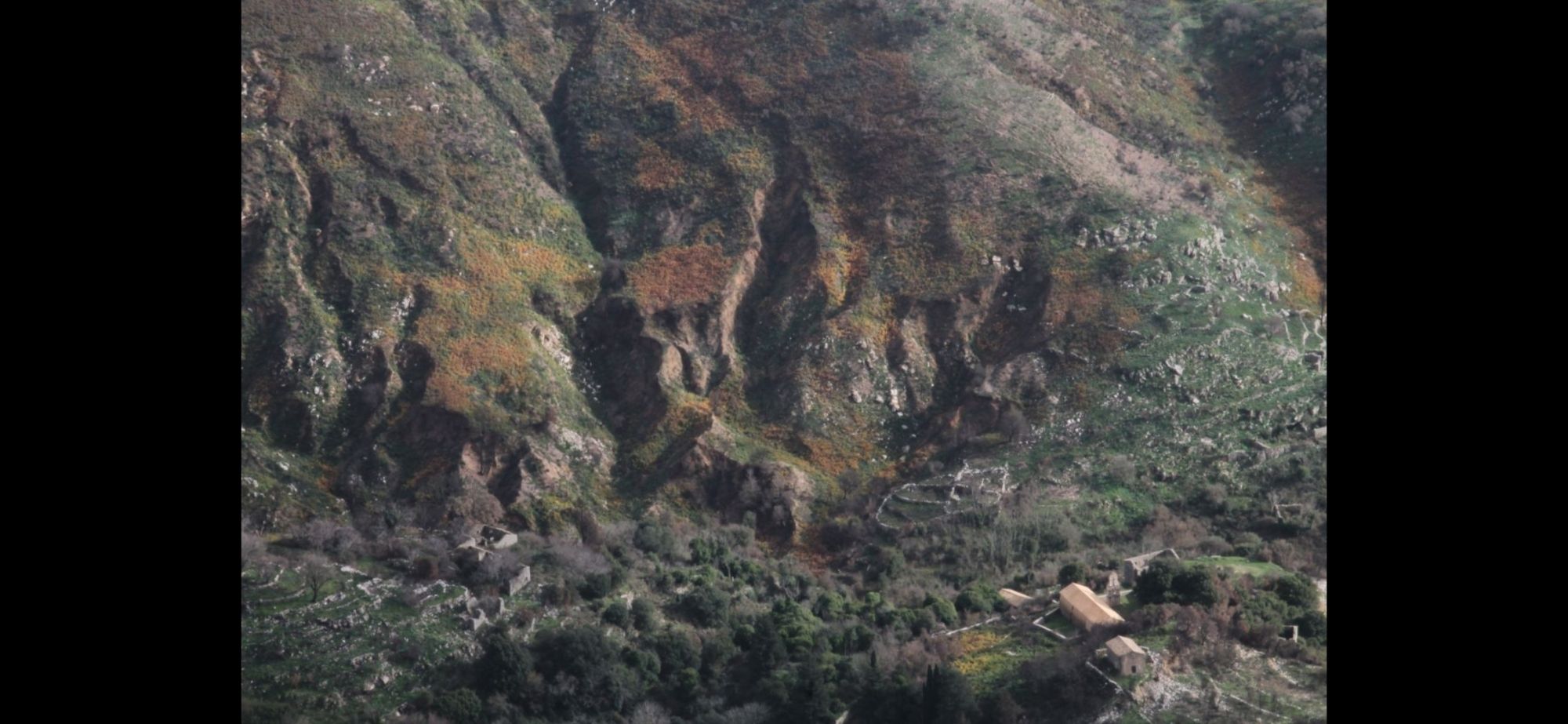 Vue d'un flanc de montagne avec roches et végétations vertes et oranges