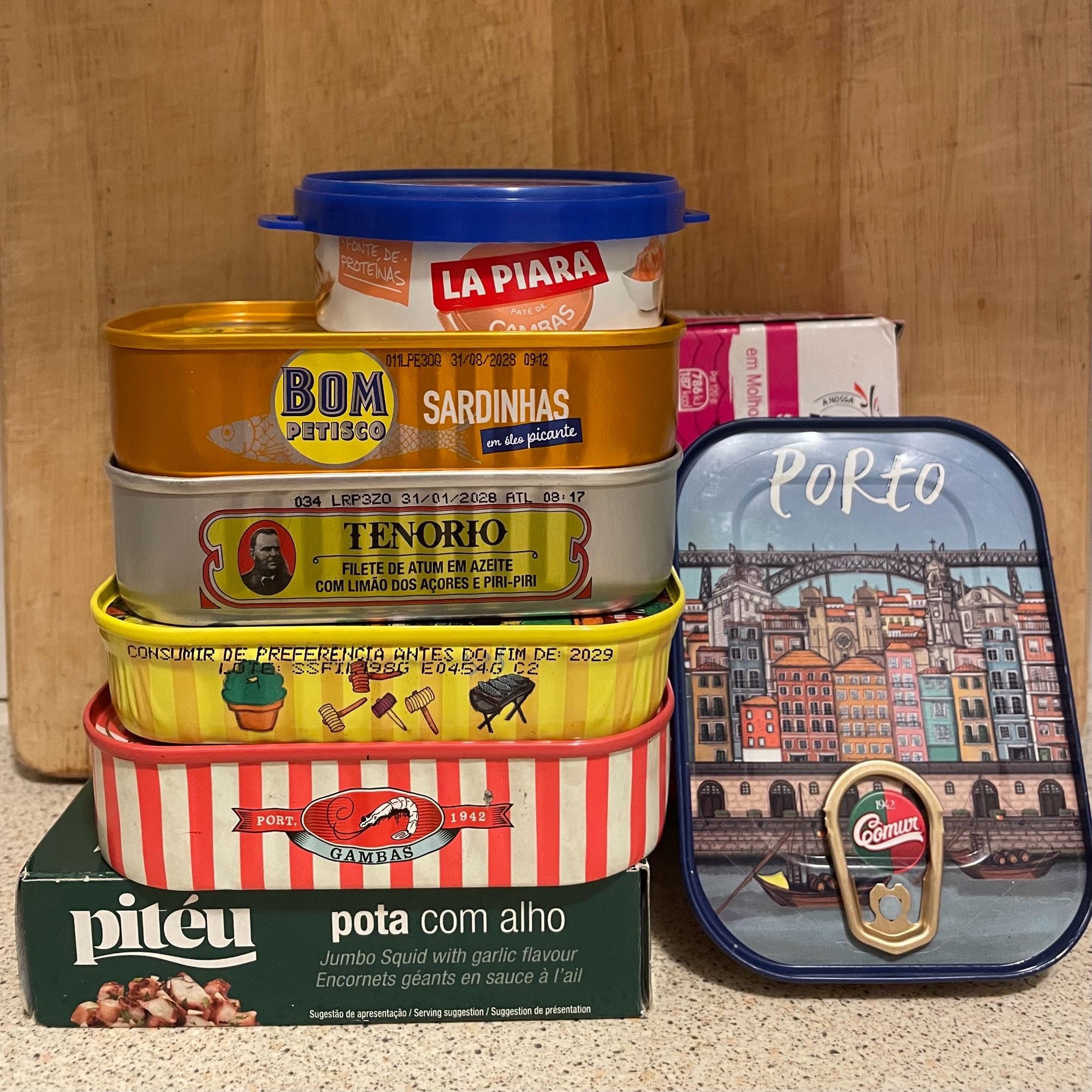 A stack of 8 colourful tins containing sardines or other seafood. One has a cartoony image of Porto on the lid.