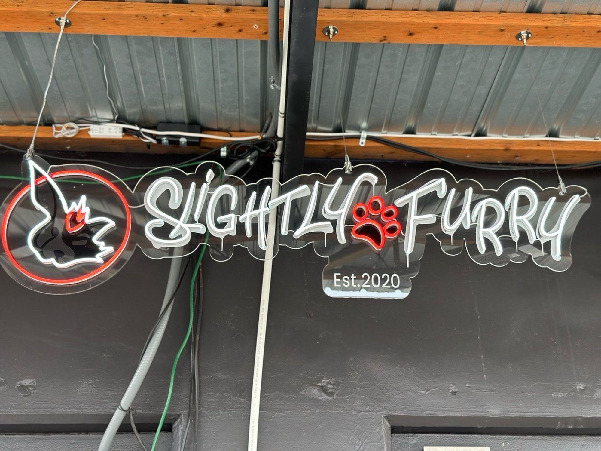 Picture of a LED sign in the shape of the Slightly Furry company logo with a paw and the signature fox and bunny face on the left. “Established 2020”