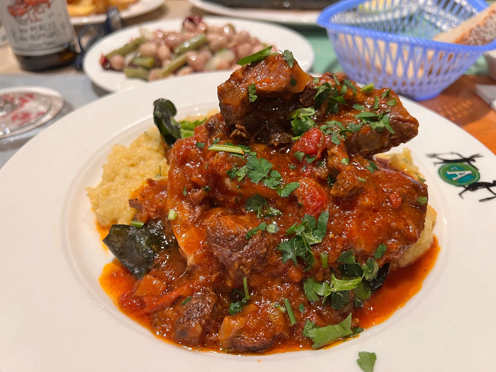 Bord met eten. Vlees in rode saus + polenta + groene verse kruiden