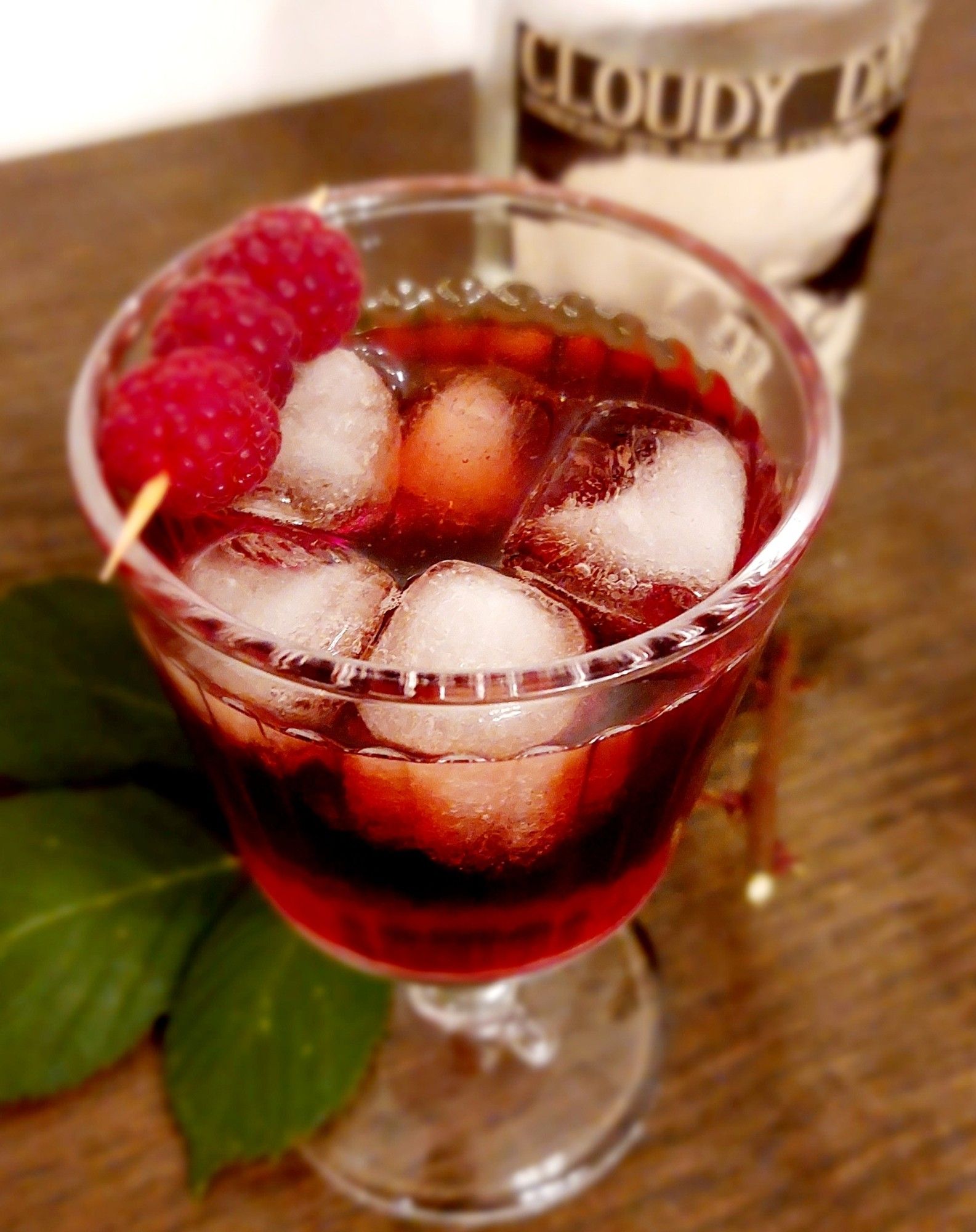 Ein tiefroter Cocktail mit Eiswürfeln und ein paar Himbeeren als Garnish.