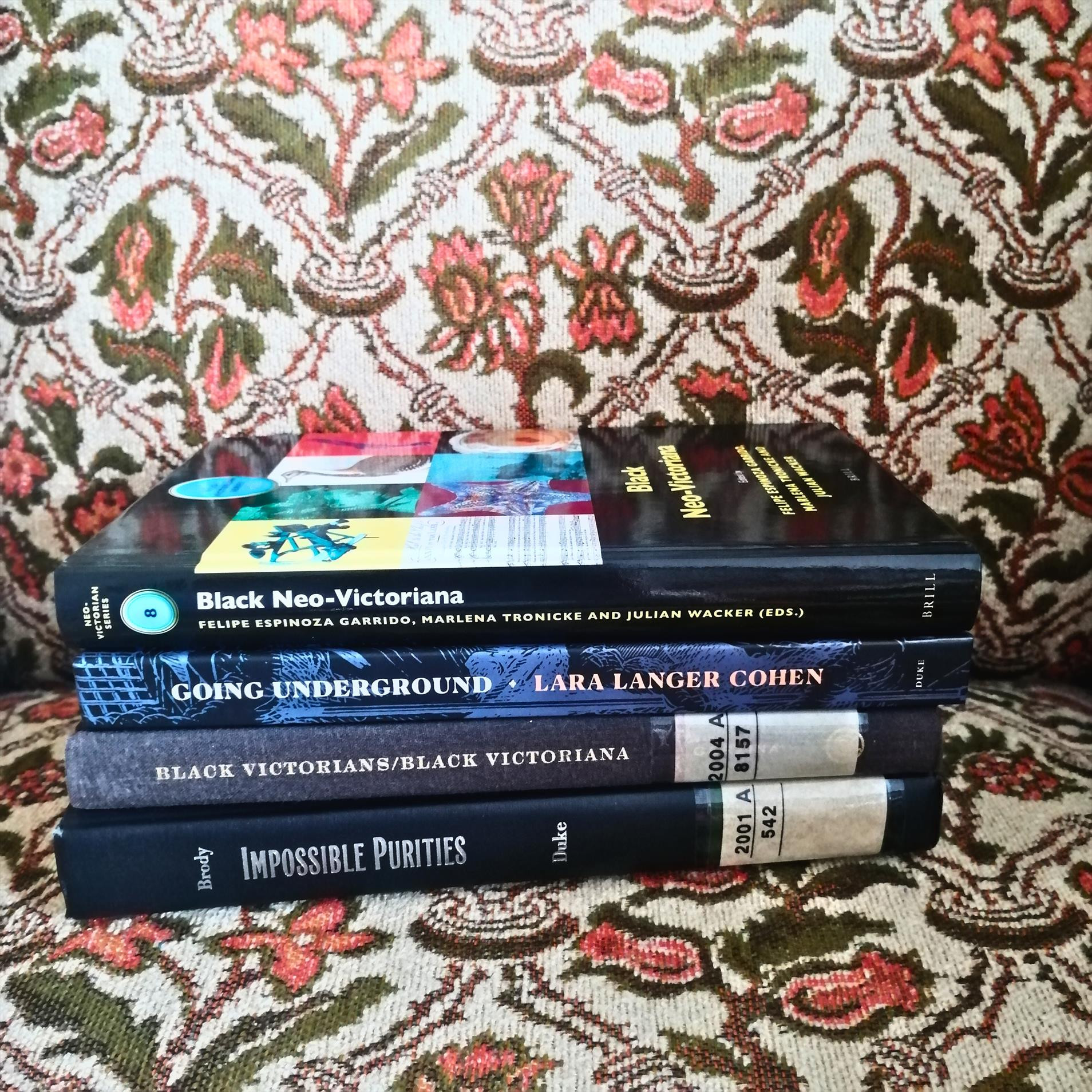 a bookstack of 4 books on Black people in history & fiction of the 19th century, resting on a vintage chair