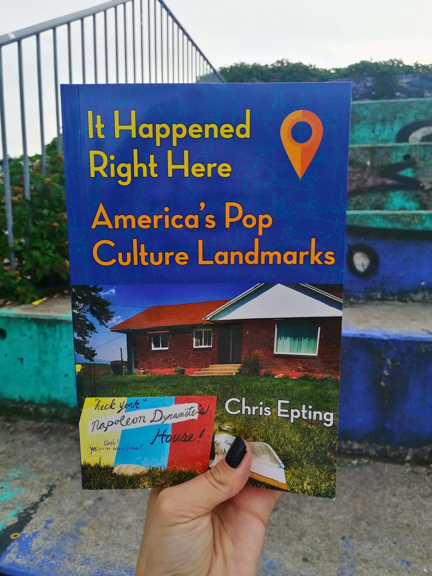 Holding the book "It Happened Right Here: America's Pop Culture Landmarks" in front of a graffiti-ed concrete staircase on Göttingen campus