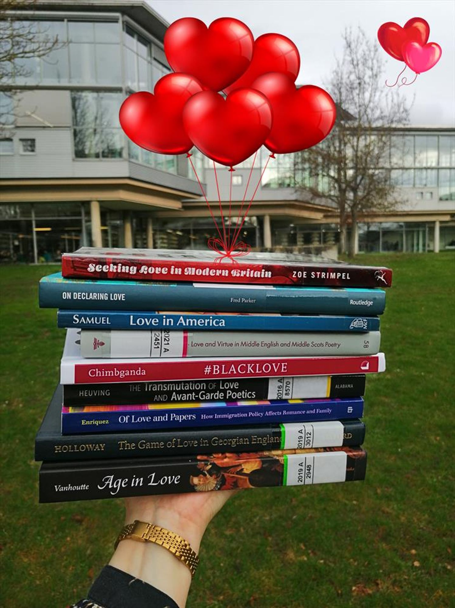 A pile of books outside of SUB Göttingen, with images of heart-shaped helium balloons in a bright red tied to them, as if to lift them up