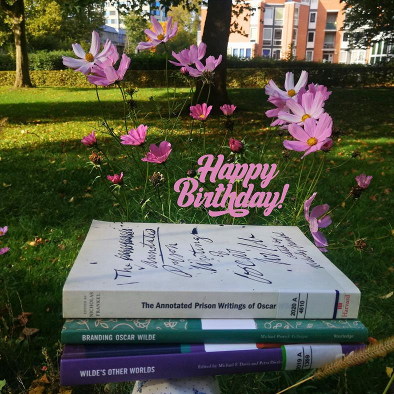 a pile of 3 books in front of a wildflower meadow at SUB library, with the phrase "Happy Birthday" in pink written in the picture