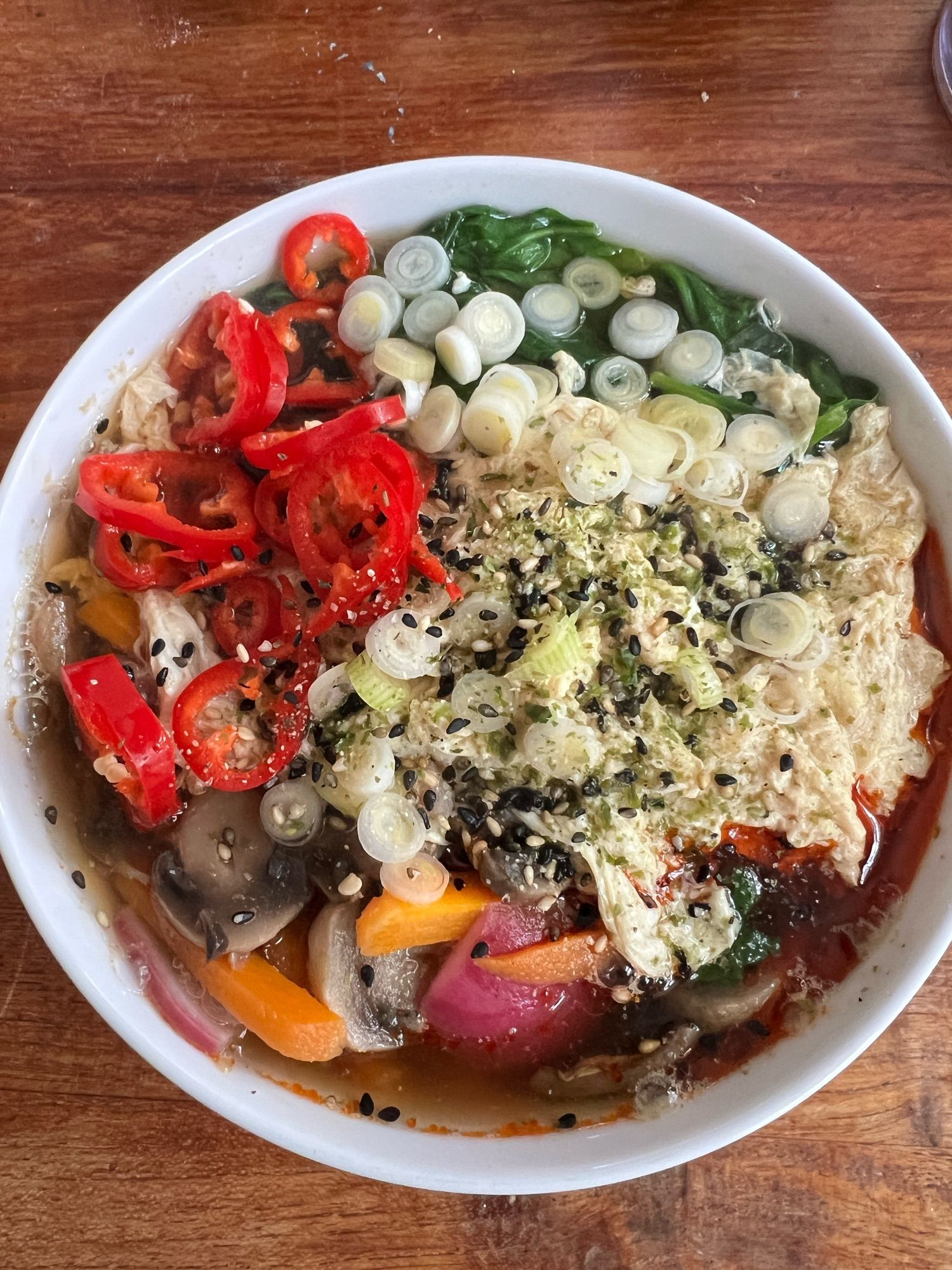 A bowl of soba noodle soup with fresco peppers, scallions, furikake, and egg on vegetables.