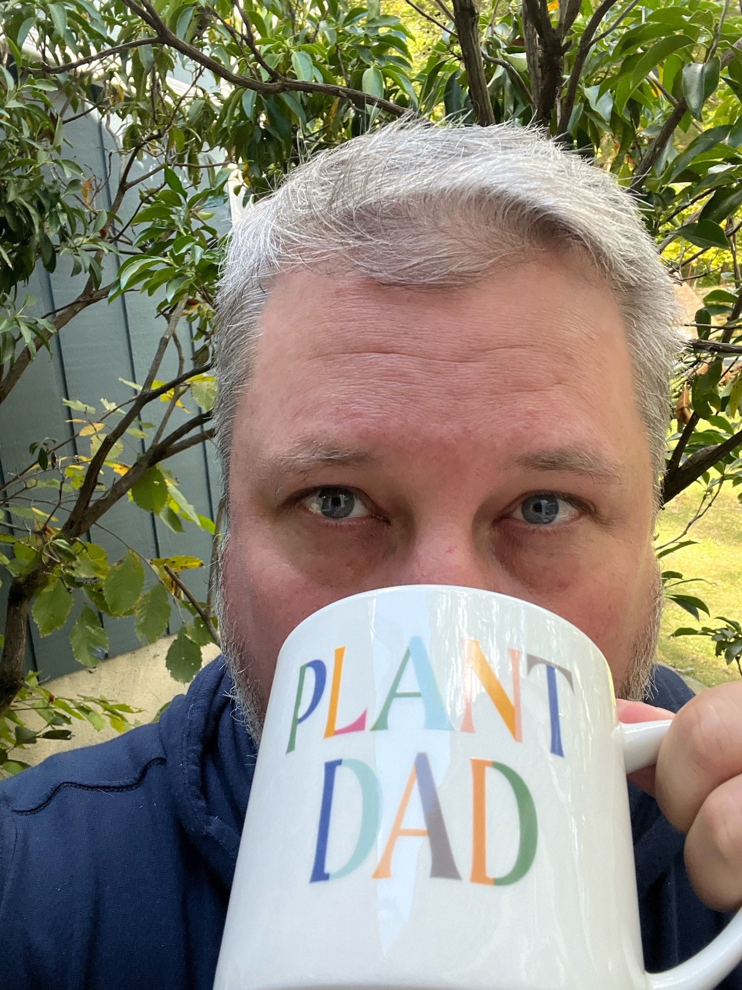 A man sipping tea from a mug that says ‘plant’ dad “.