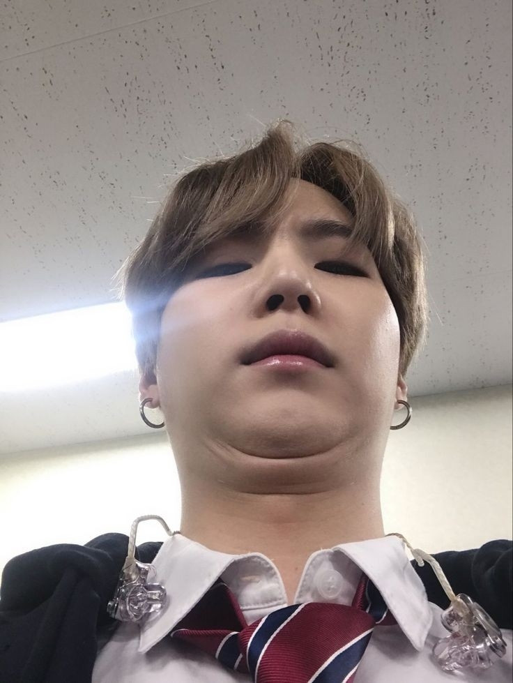 yoongi's selfie taken from a low and weird angle where he looks at the camera a little bit confused. He has a funny face.