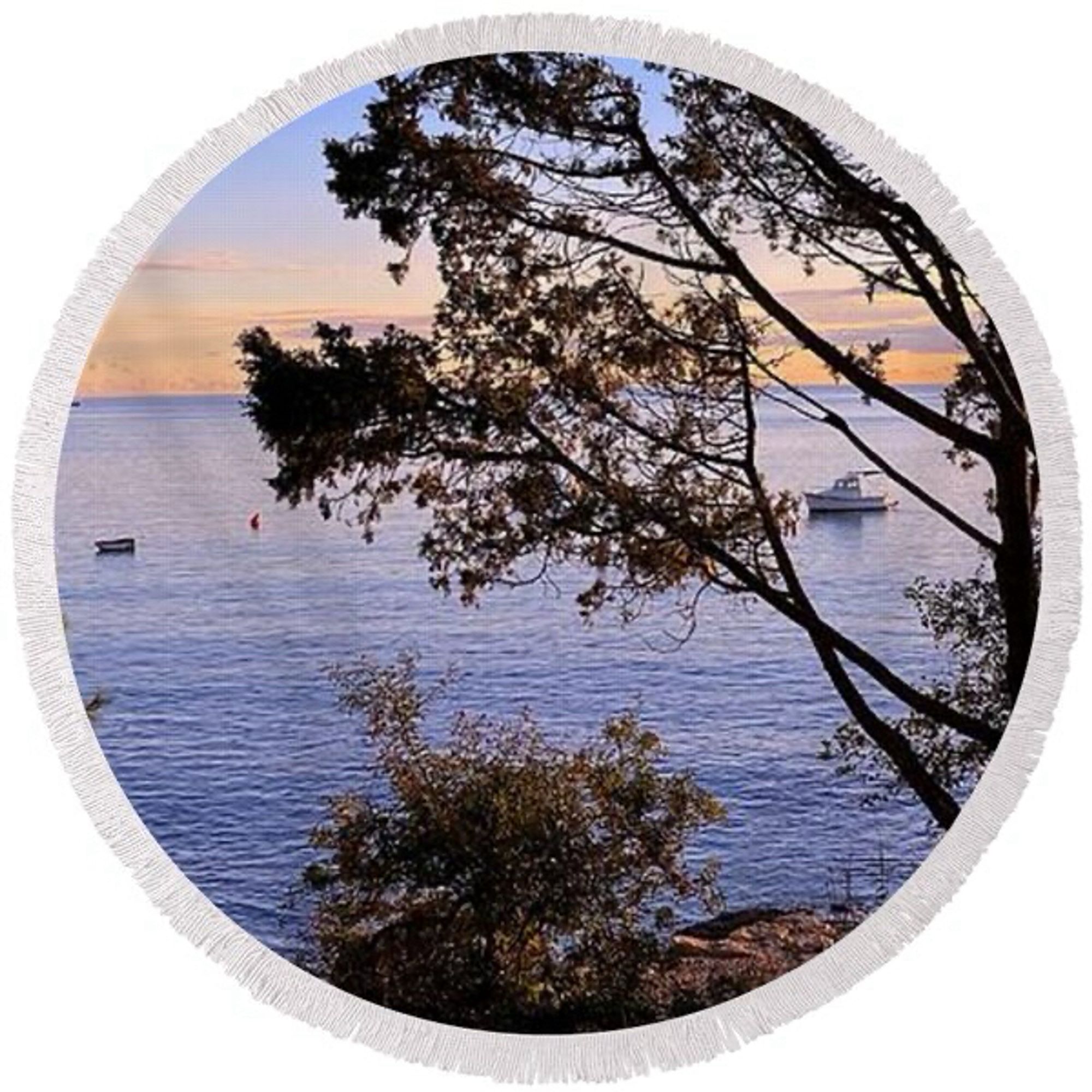 Round beach towel depicting a bay with a floating boat that is visibke through the branches of a tree.