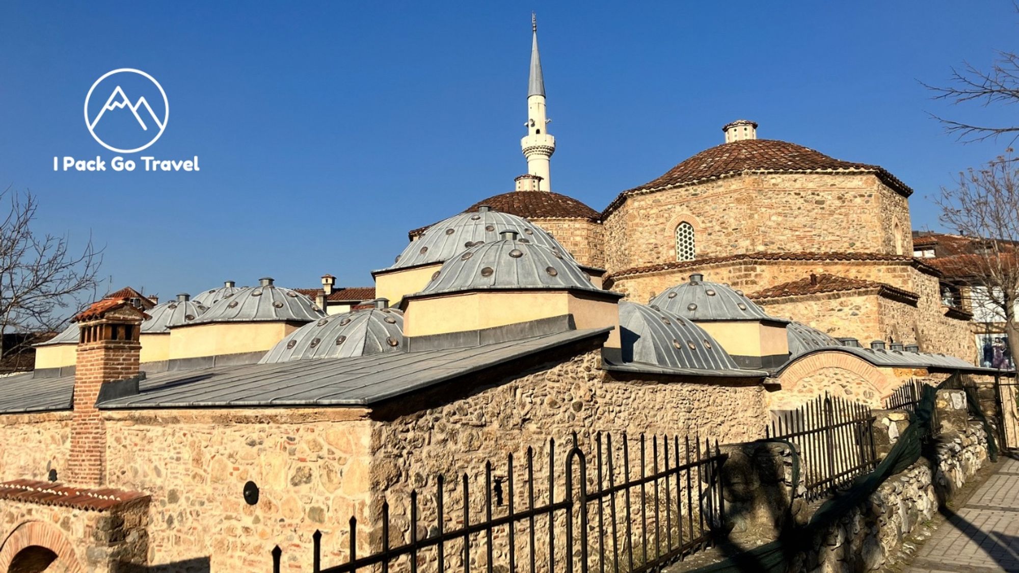 Historical stone buildings with domed-shaped roofs. There is a white Mosque Tower and a blue sky in the background.