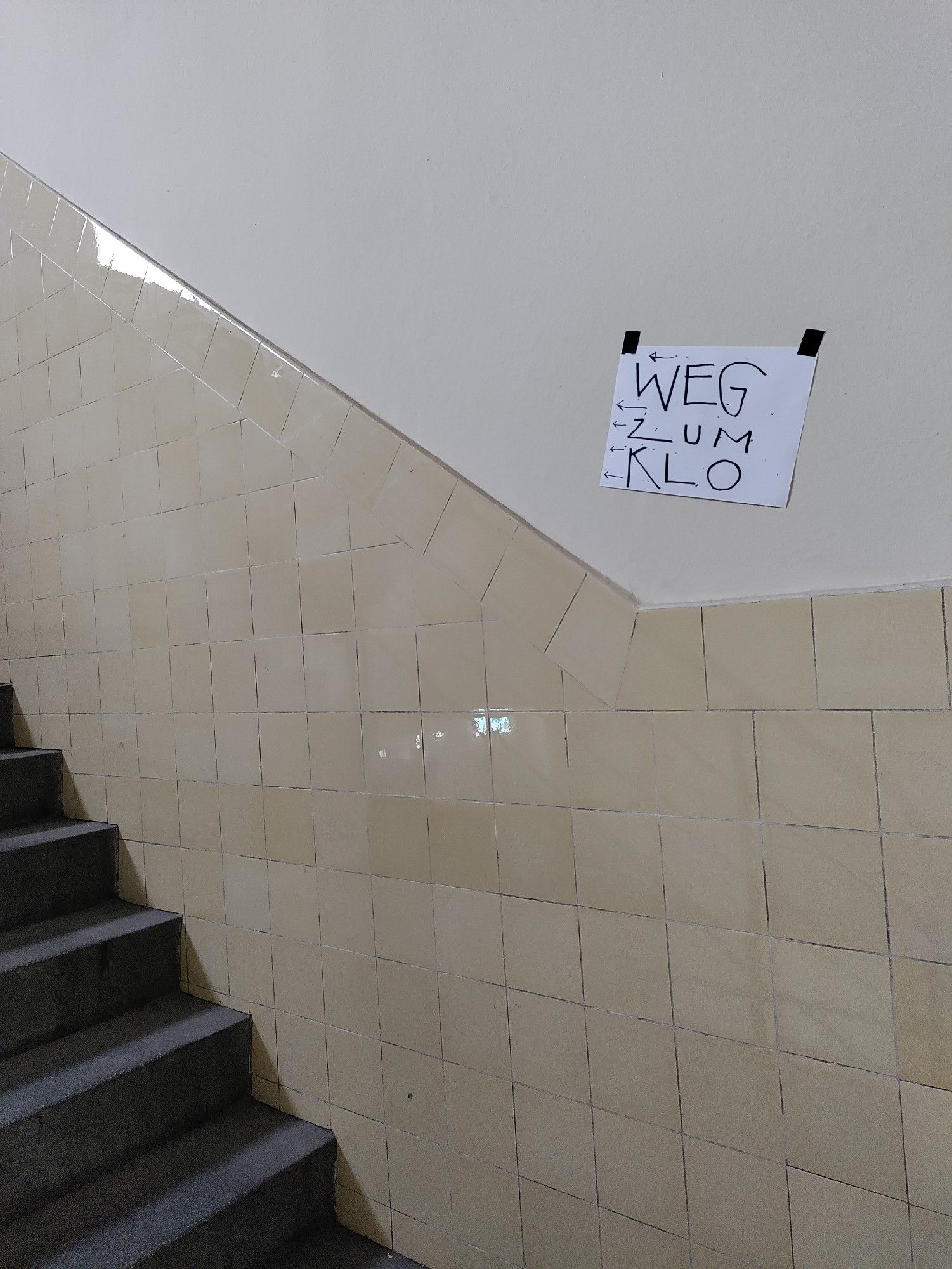 Treppenhaus mit Schild das nach oben zeigt "Weg zum Klo"