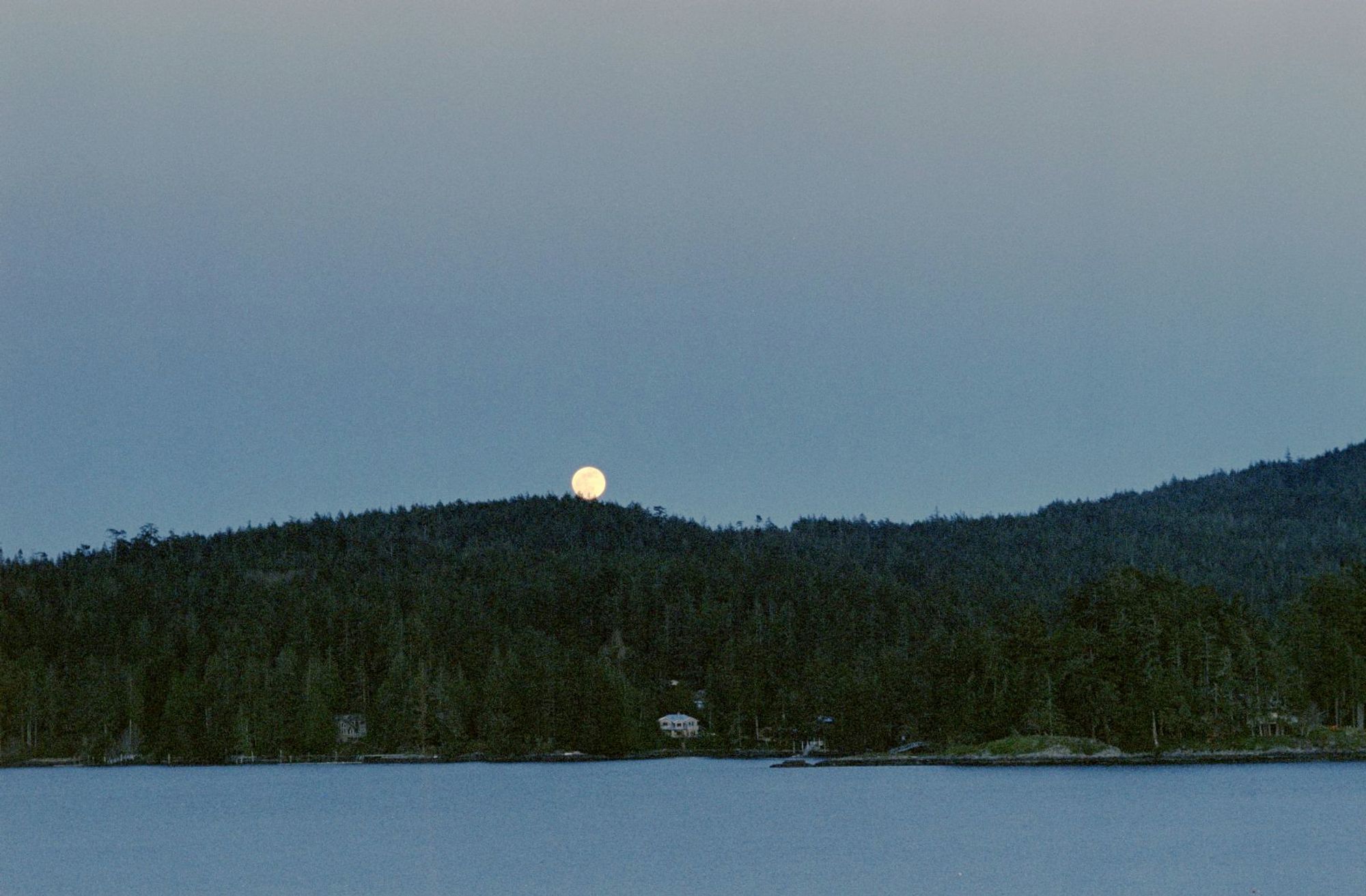 A photo of a moon rise over a distant hill across a body of water