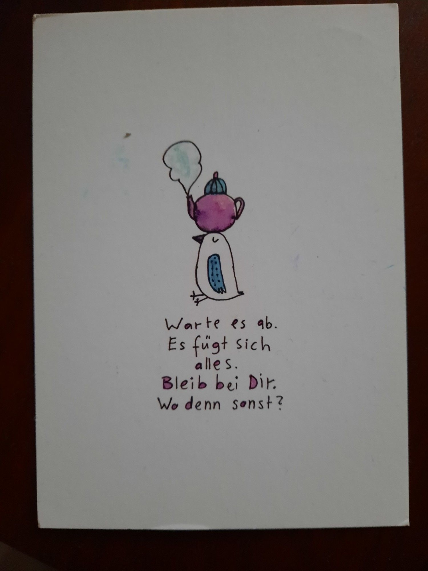 Eine Postkarte, auf der ein gezeichneter Vogel eine gezeichnete Teekanne auf dem Kopf hat.
Darunter steht:
Warte es ab. Es fügt sich alles. Bleib bei Dir. Wo denn sonst?