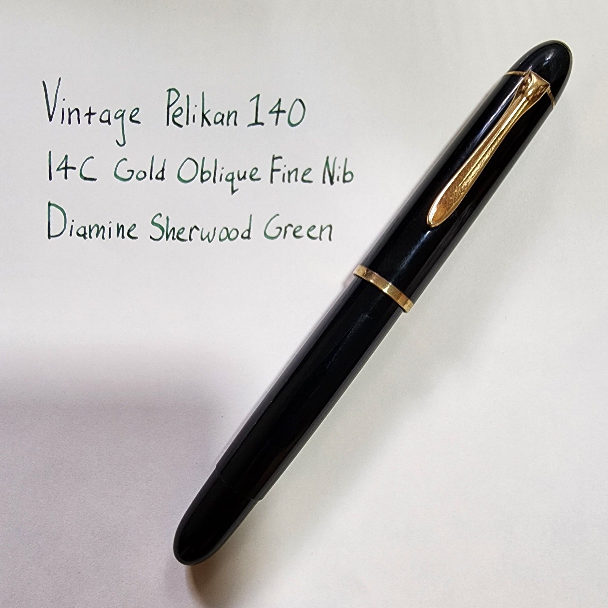 A vintage Pelikan 140 fountain pen (capped) on a piece of paper. There is text handwritten on the paper:
Vintage Pelikan 140
14C Gold Oblique Fine Nib
Diamine Sherwood Green