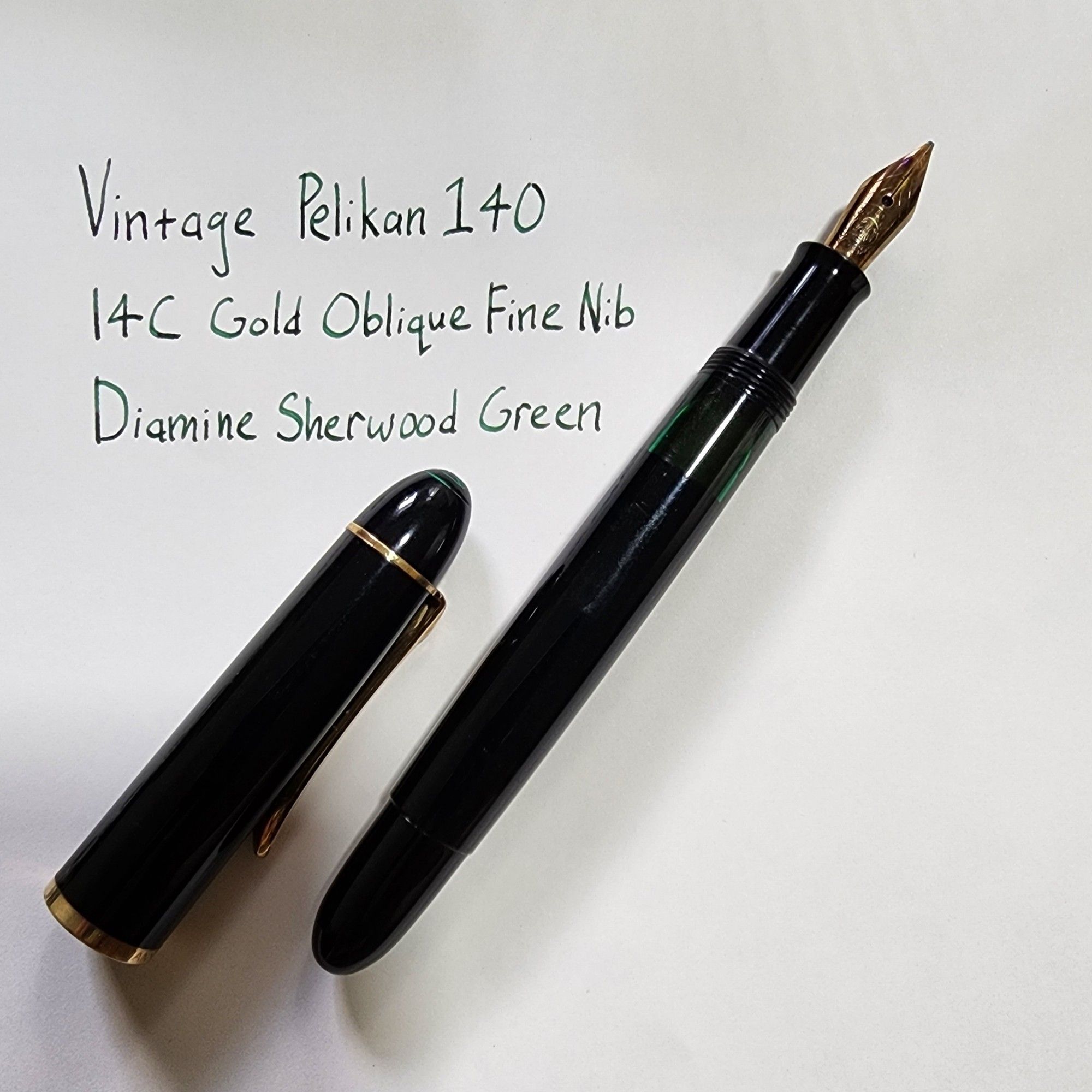 A vintage Pelikan 140 fountain pen (uncapped) on a piece of paper. There is text handwritten on the paper:
Vintage Pelikan 140
14C Gold Oblique Fine Nib
Diamine Sherwood Green