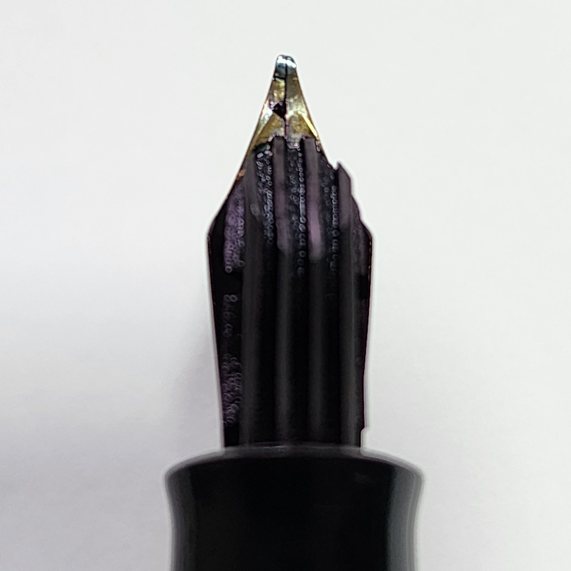 Close up of the back of the nib m of a Pelikan 140 fountain pen. The feed of the pen is black with longitudinal fins. The tip of the nib has a slight yet visible angle i.e. oblique