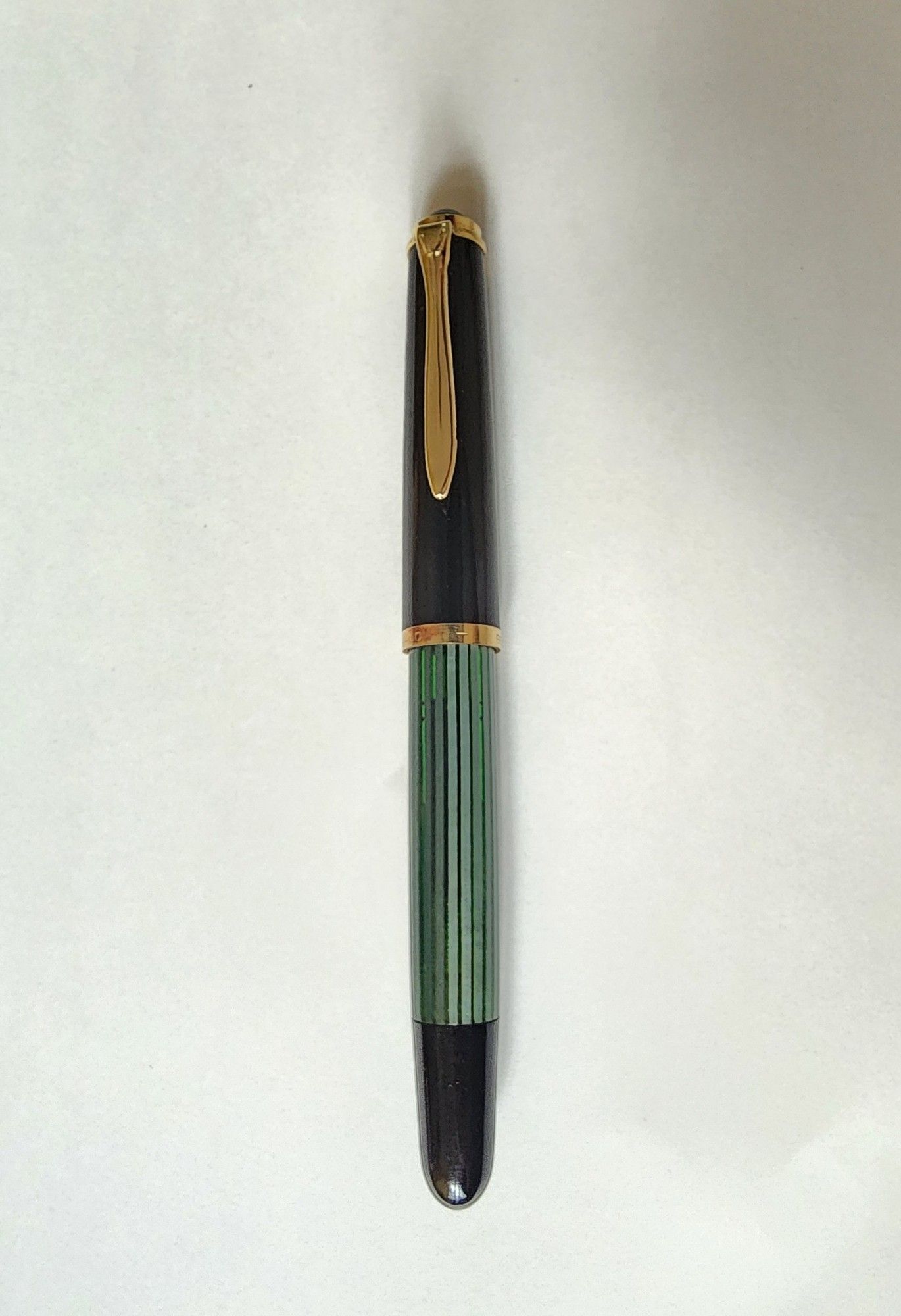 A vintage Pelikan with a black cap and piston knob, green-and-black striped barrel, and gold trim