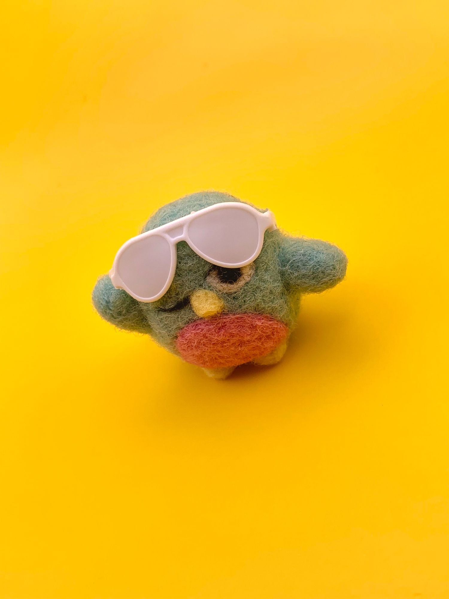 A felted penguin winking while lifting up her sunglasses from her eyes