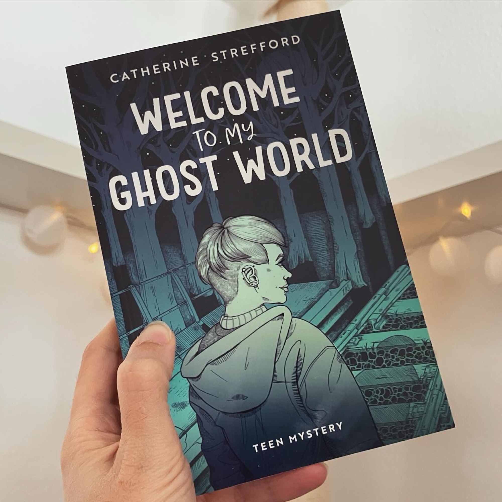 Eine Hand hält das Buch "Welcome to my Ghostworld" von Catherine Strefford in die Höhe.