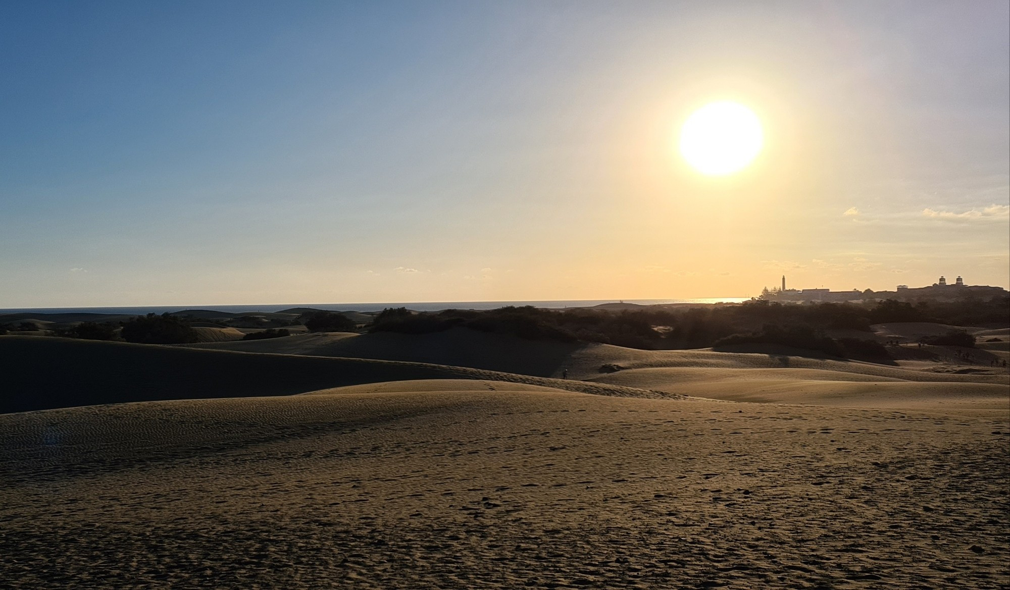 Sun going down over the Maspalomas dunes and warm sea with lighthouse in the distance