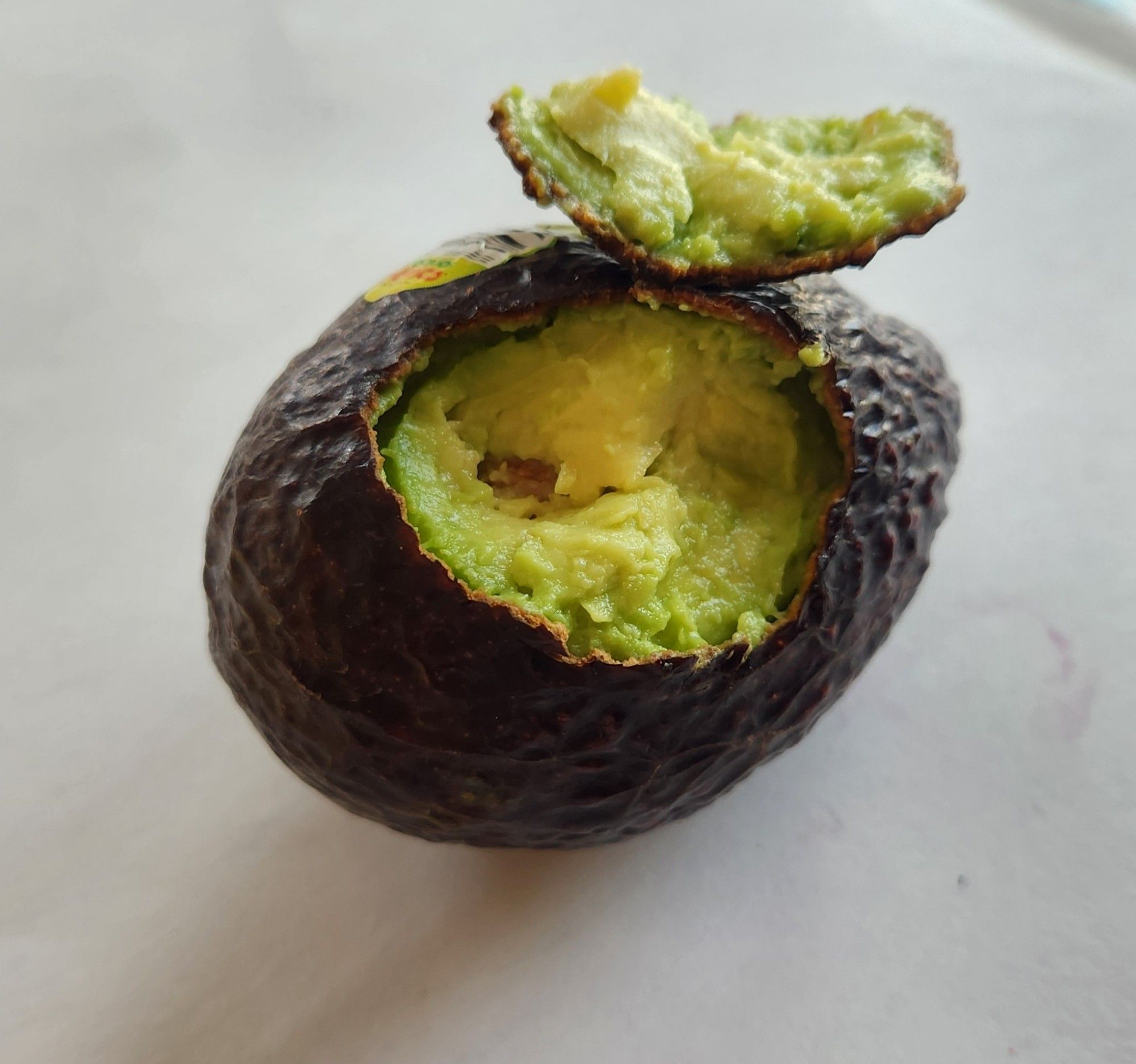 A photo of a perfectly ripe avocado with its skin ripped open by what appears to be a bitemark made by a very small person.