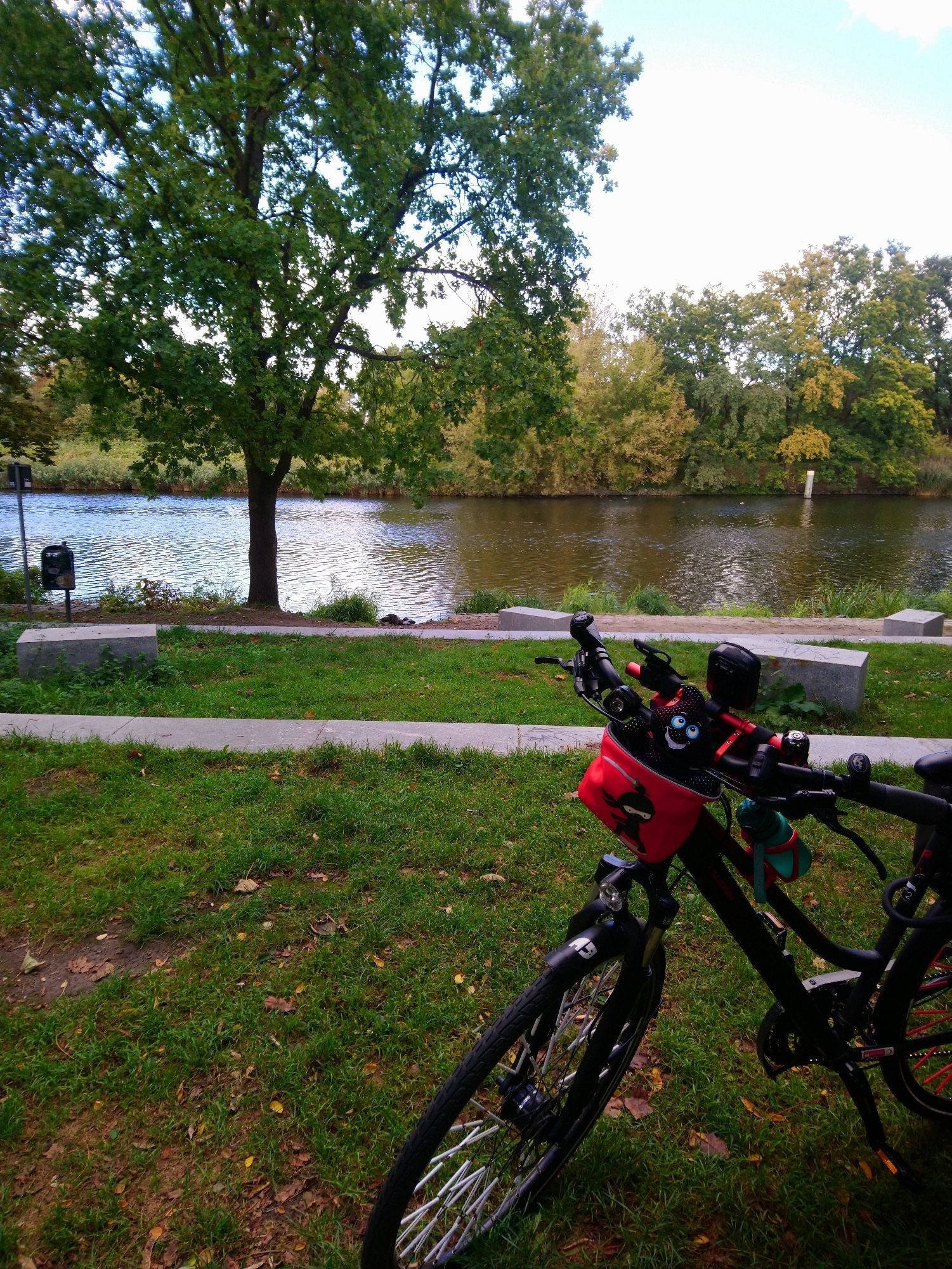 Fahrrad steht am Teltow Kanal. Am rad eine rote Lenkertasche in der ein schwarzes Plüsch Gespenst sitzt