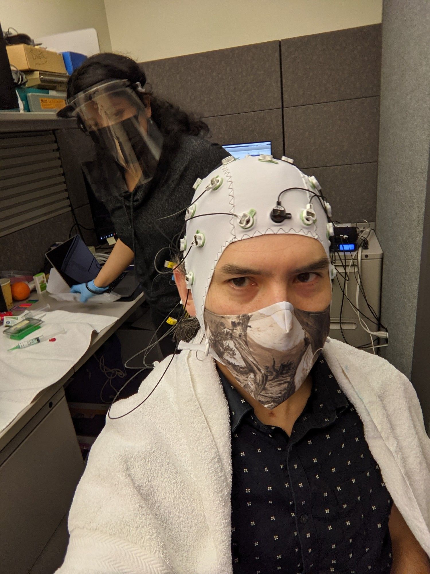 Haydée García-Lázaro and Santani Teng doing an EEG experiment in the lab with Santani being the participant wearing an EEG net and Haydée running the experiment.