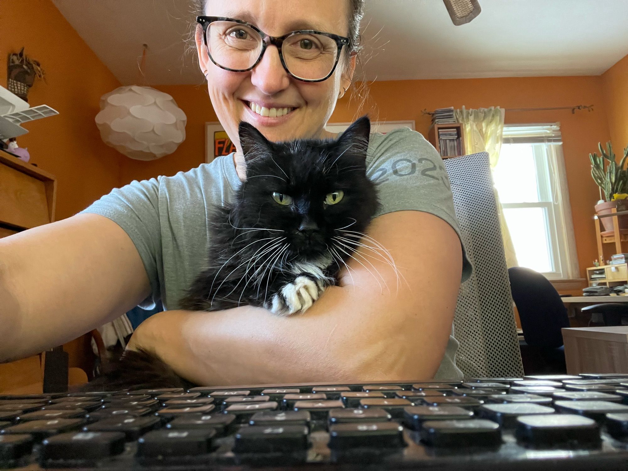 Lara with Cookie a black and white cat on her lap in front of a keyboard.