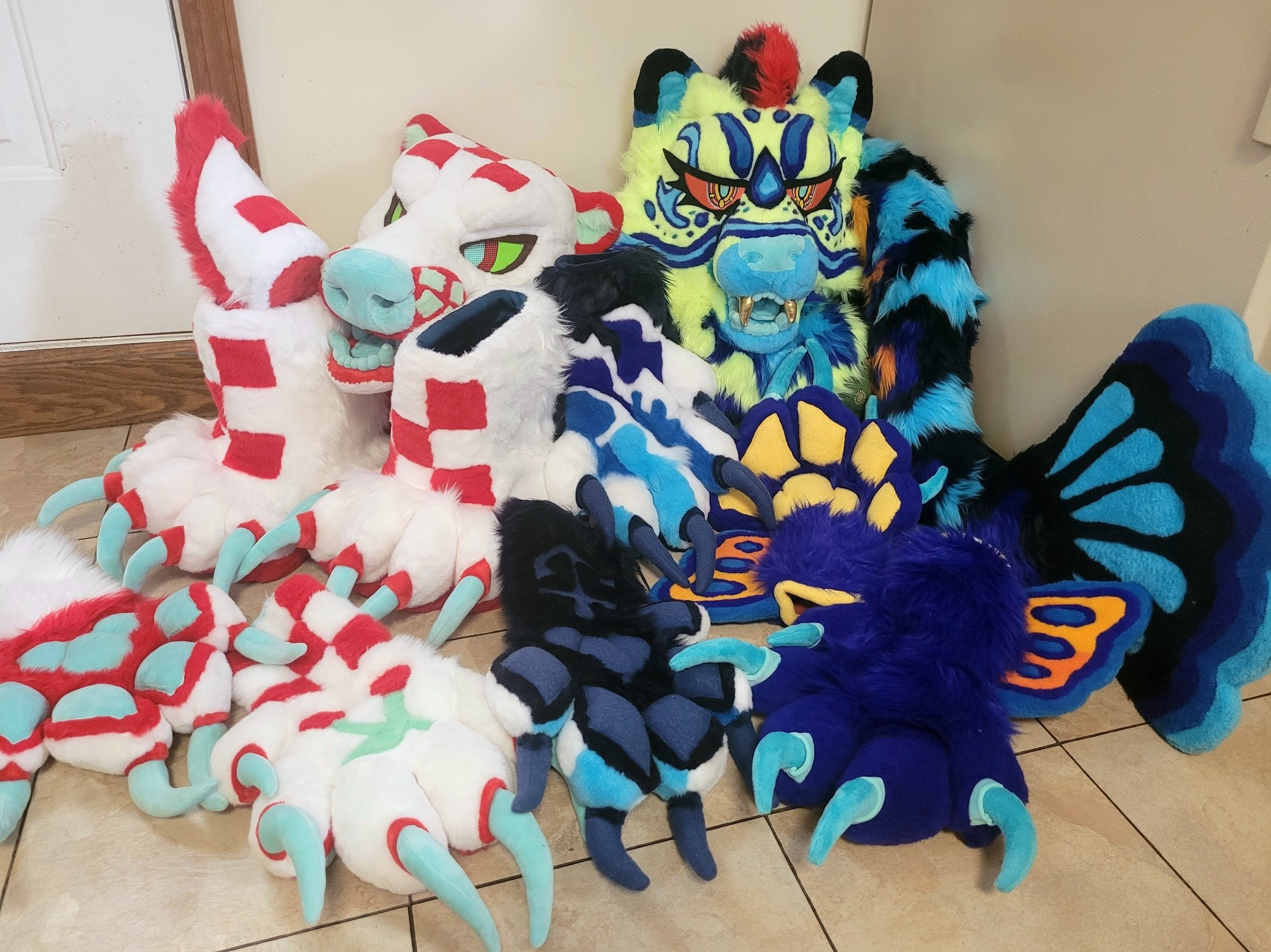 A photo of two fursuits side by side. One is a white and red picnic bear. The other is a yellow and blue cheetah fish