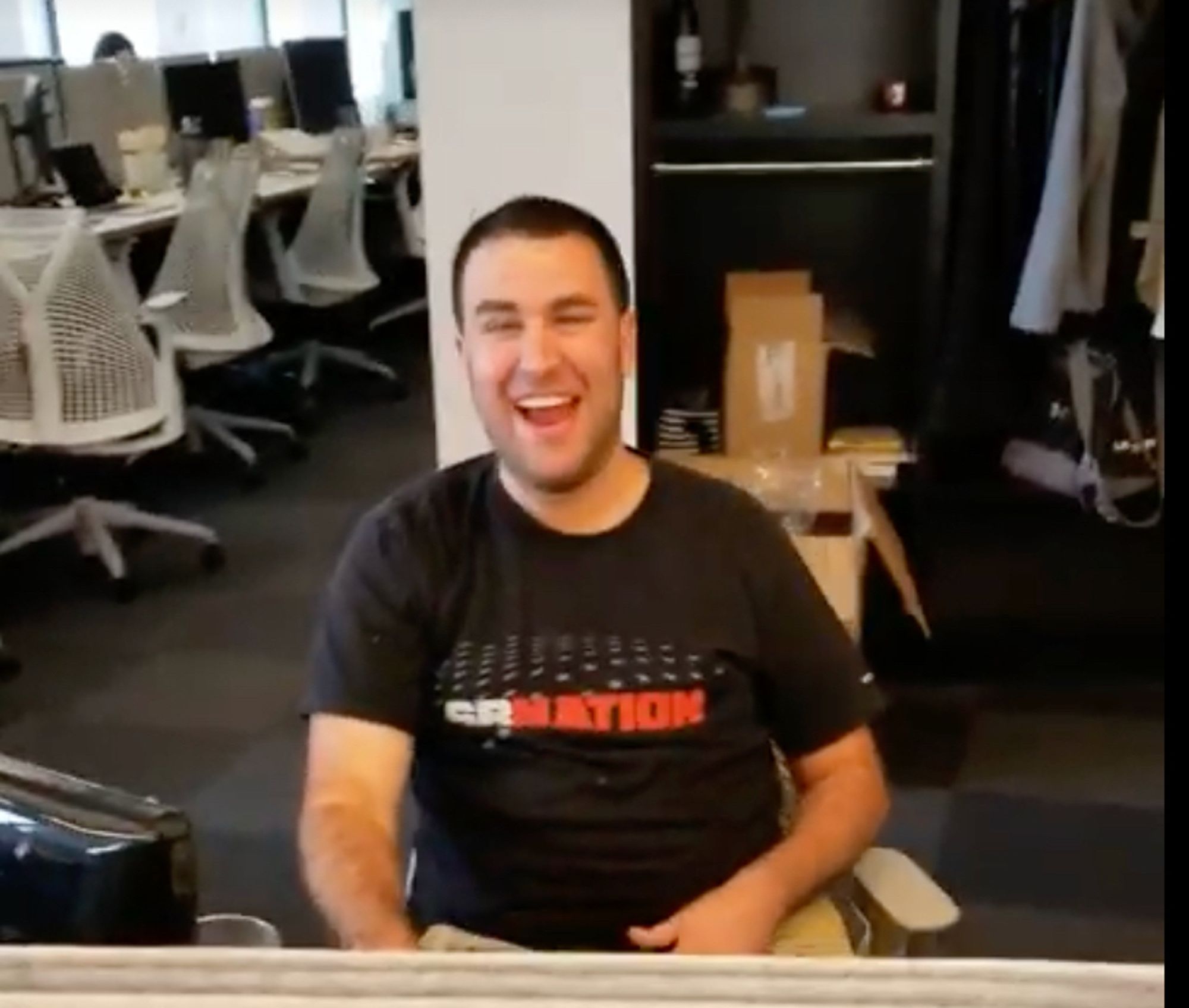 A person laughs in reaction to a longform commercial's brand. He is wearing a black shirt and sitting in a chair.